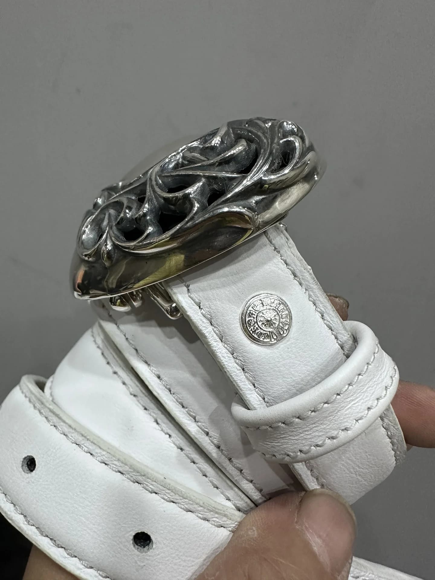 Крупный план резной пряжки-сердца и фиксирующей кнопки белого ремня Chrome Hearts