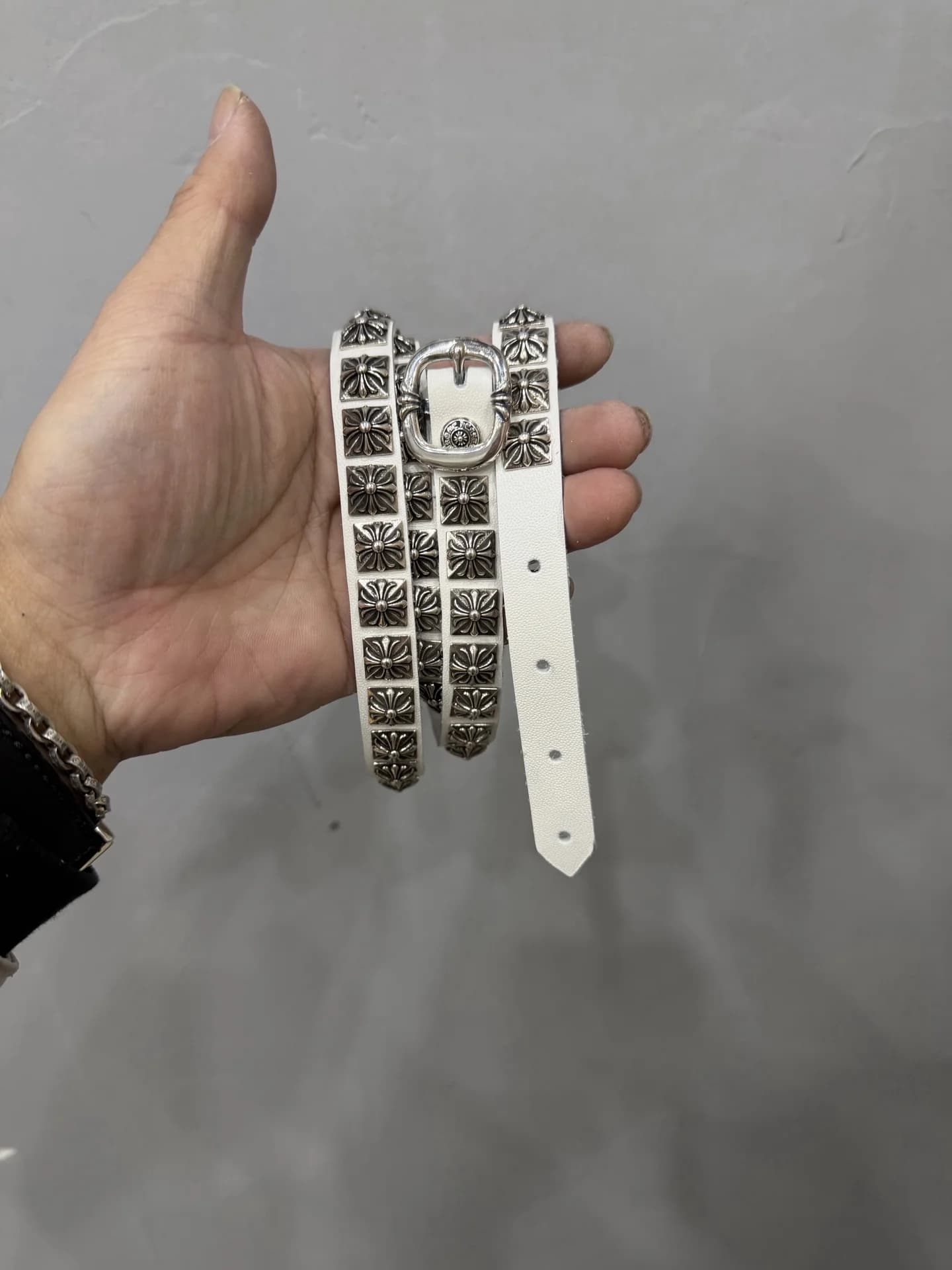 Узкий белый кожаный ремень Chrome Hearts с серебряными заклепками в руке