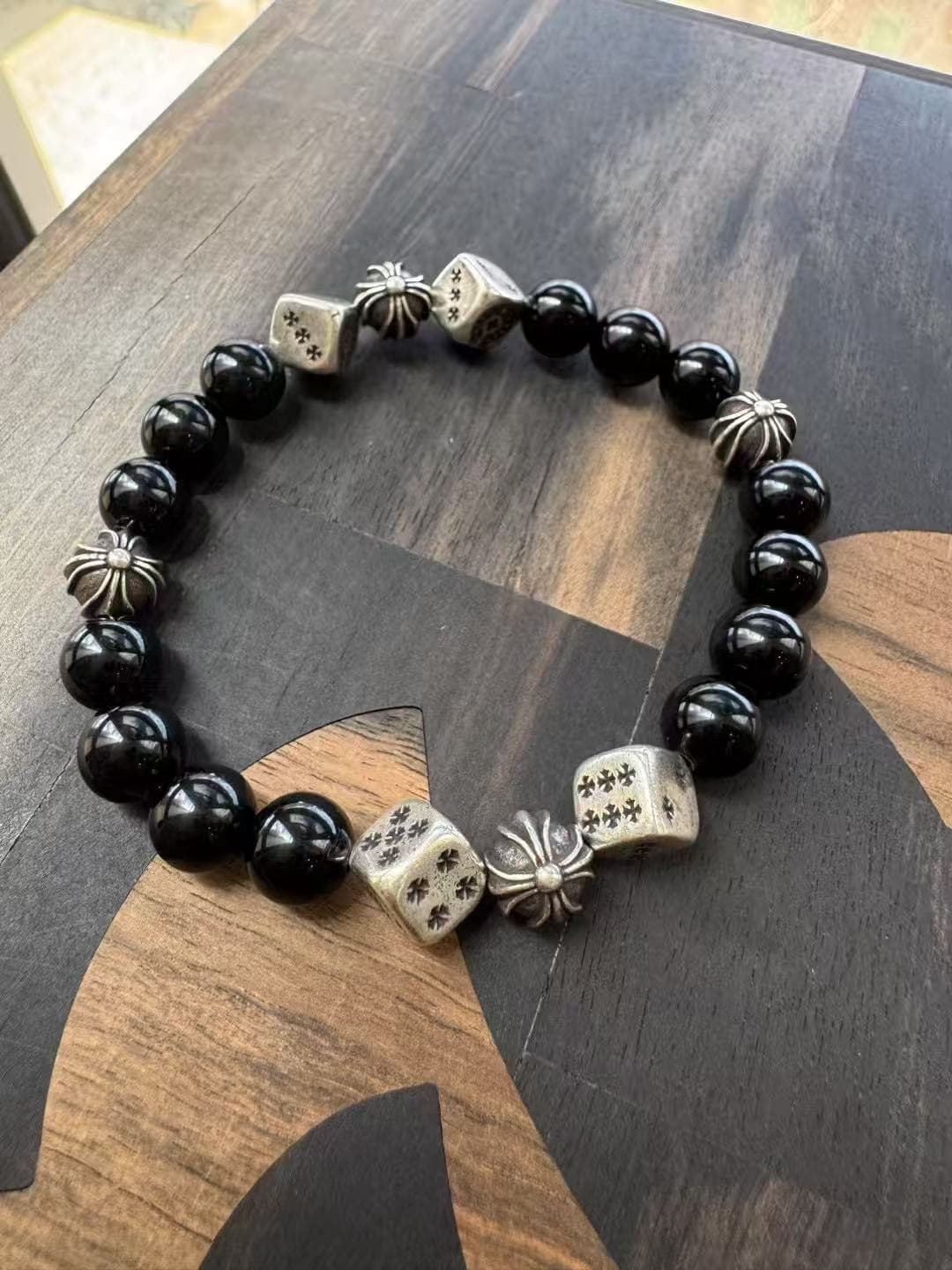 Общий вид браслета Chrome Hearts из обсидиана с серебряными вставками на деревянной поверхности