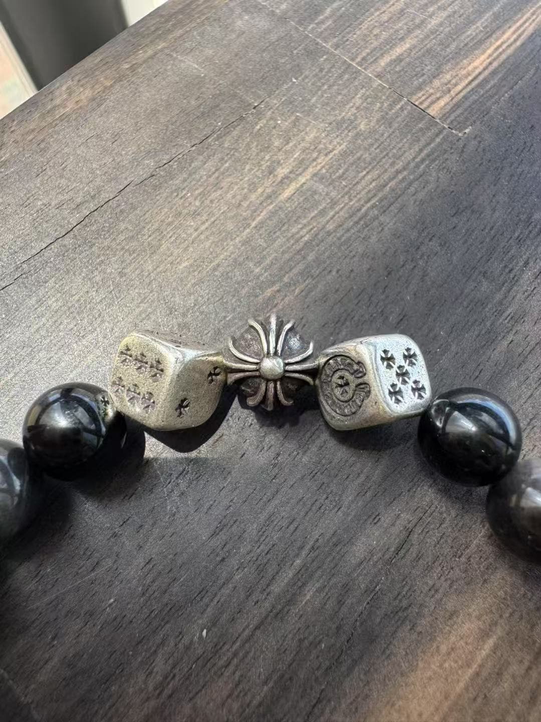 Крупный план серебряных кубиков и крестовой бусины на браслете Chrome Hearts