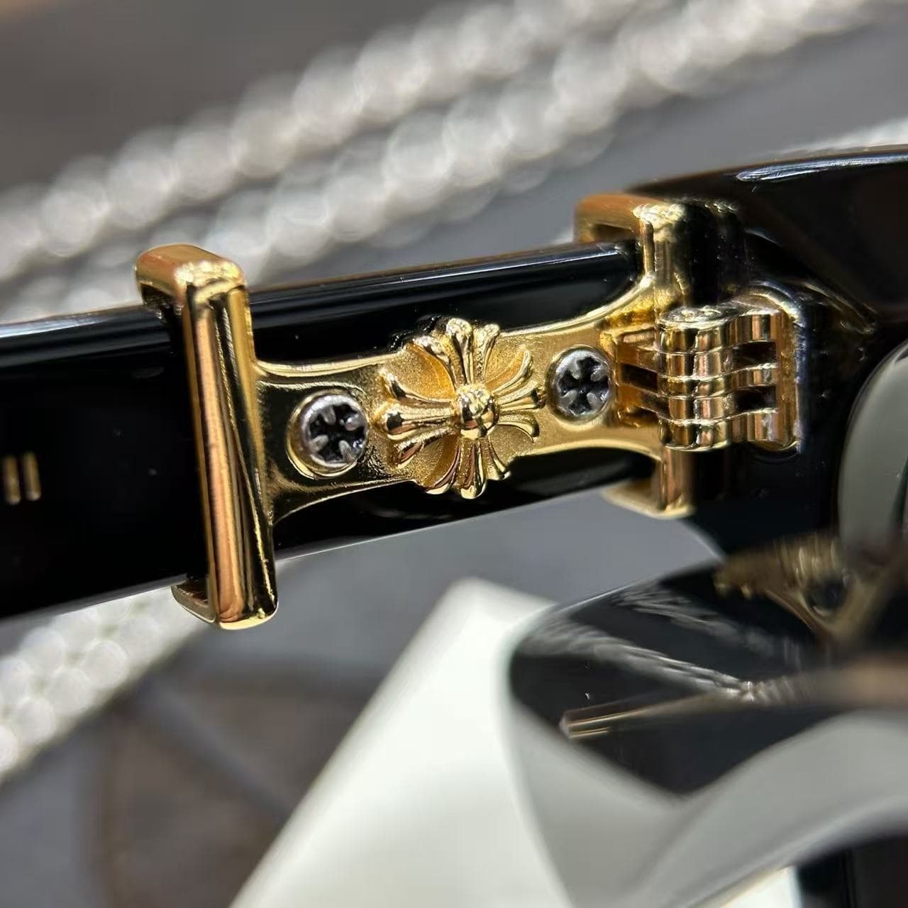 Крупный план петли и золотистого креста Chrome Hearts на заушнике оправы