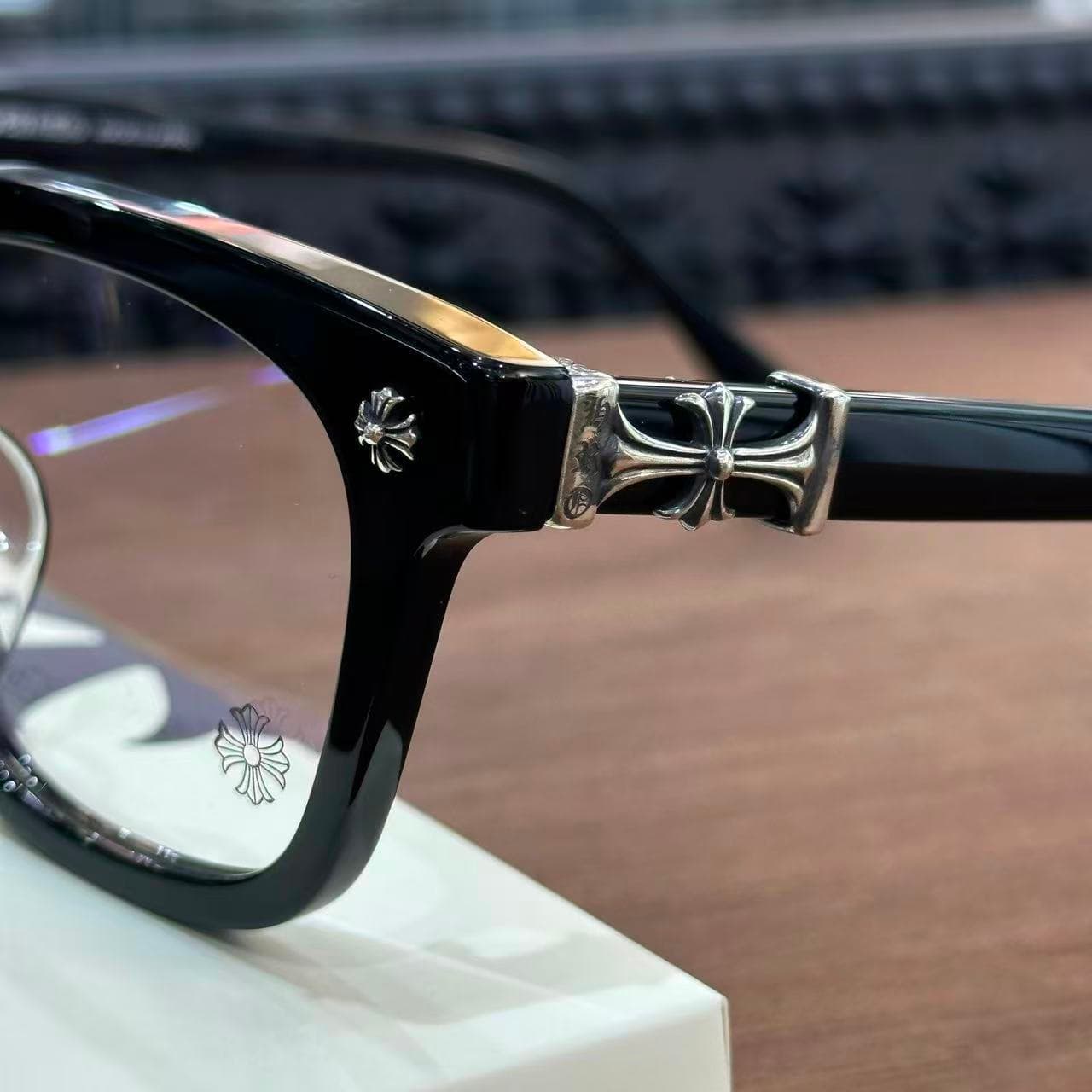 Крупный план серебряного декоративного креста на шарнире очков Chrome Hearts