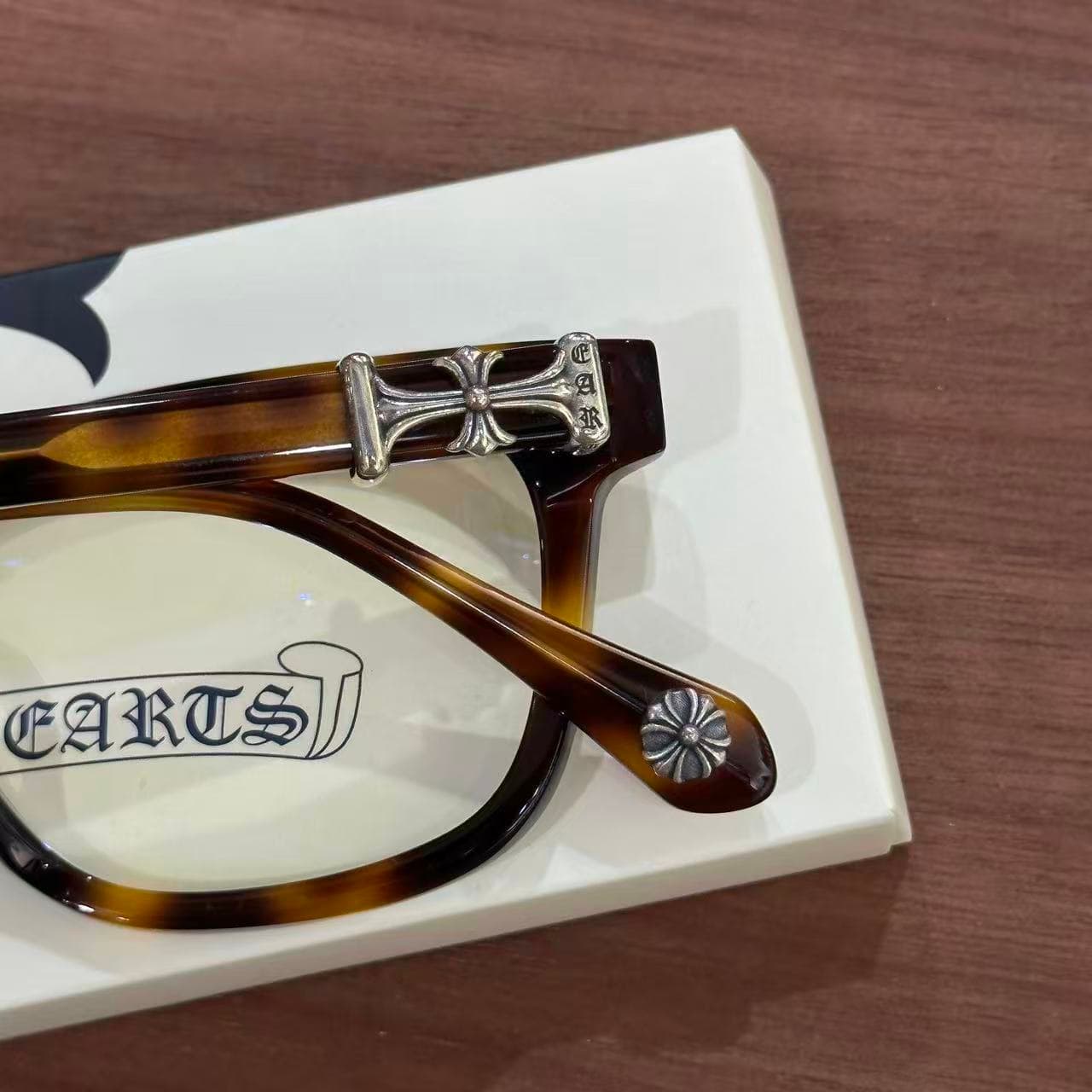 Крупный план серебряного креста Chrome Hearts на дужке очков COX UCKER
