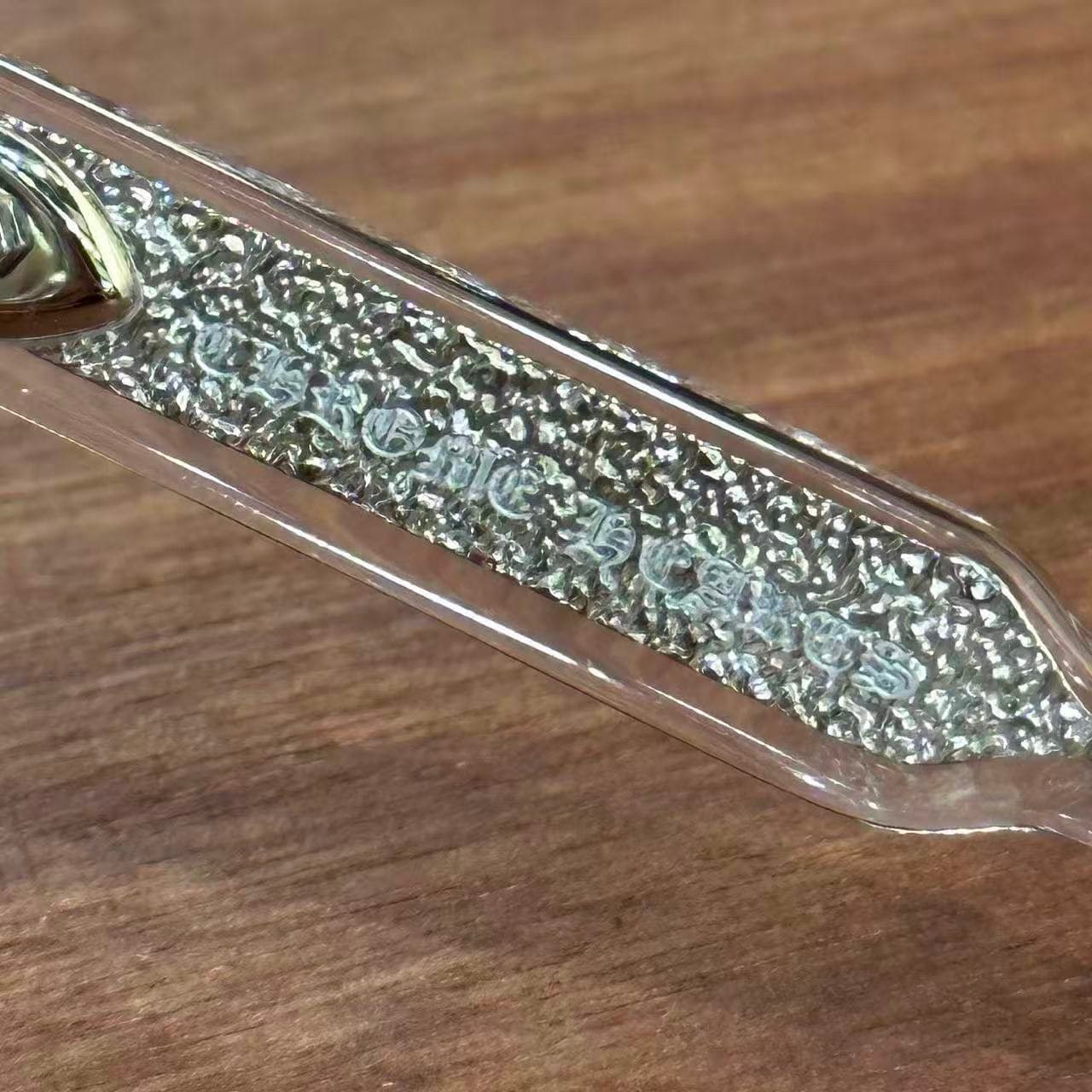 Крупный план гравировки Chrome Hearts на серебряном сердечнике дужки