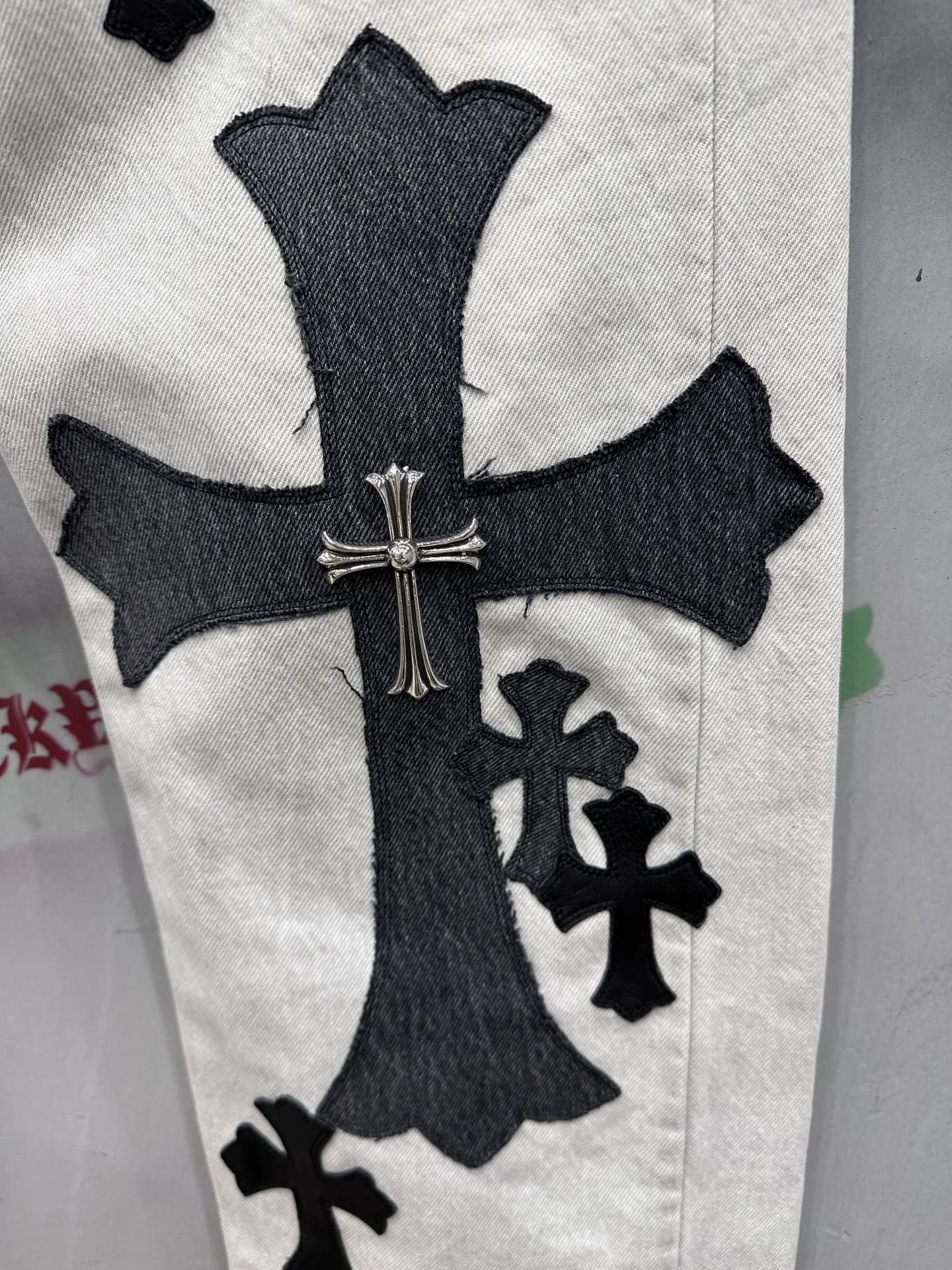 Деталь штанины джинсов Chrome Hearts с кожаной нашивкой и серебряным крестом