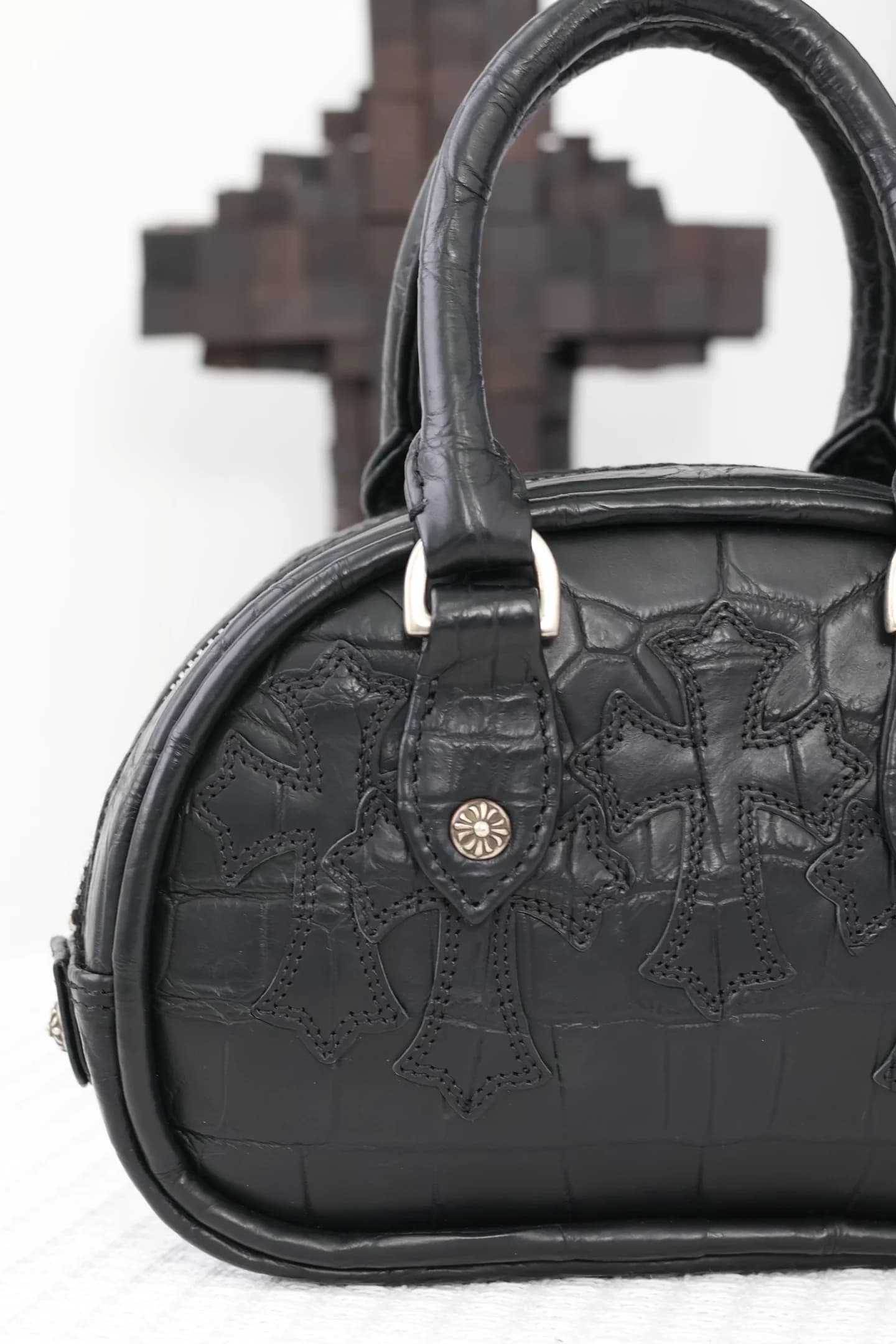 Фактура кожи крокодила и патч-крест с серебряной заклепкой на сумке Chrome Hearts