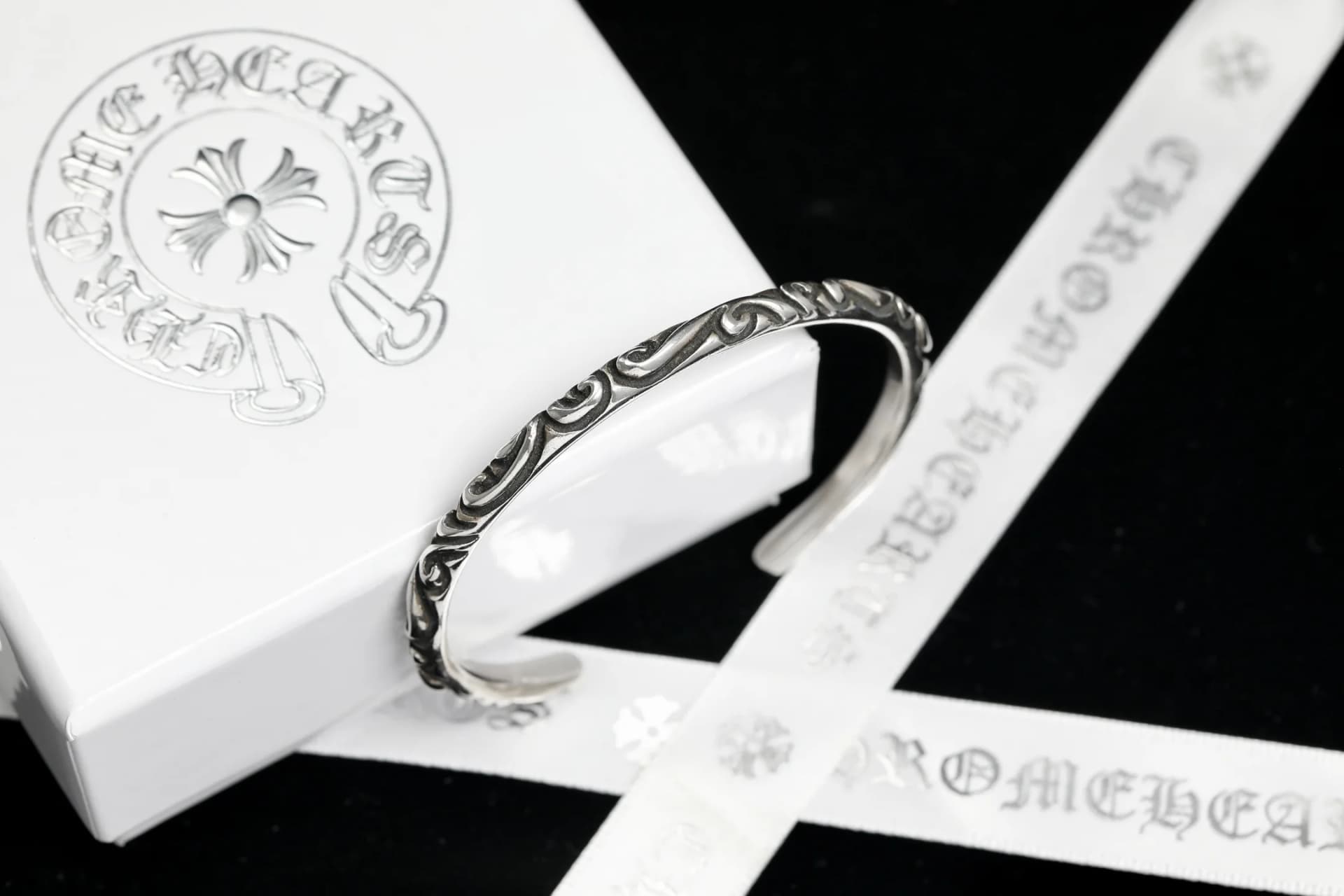 Серебряный браслет-кафф Chrome Hearts Scroll на фоне фирменной упаковки