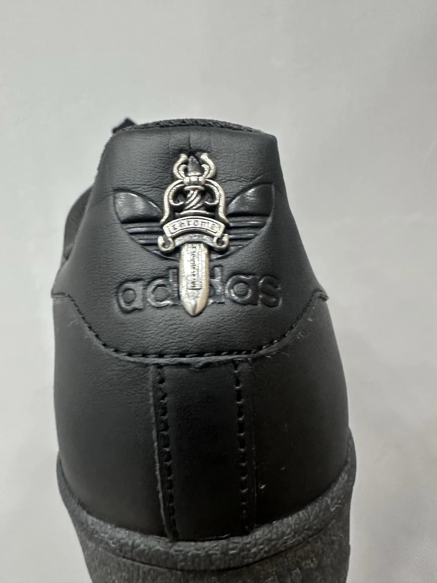 Крупный план серебряного кинжала Chrome Hearts на заднике кед Adidas Superstar