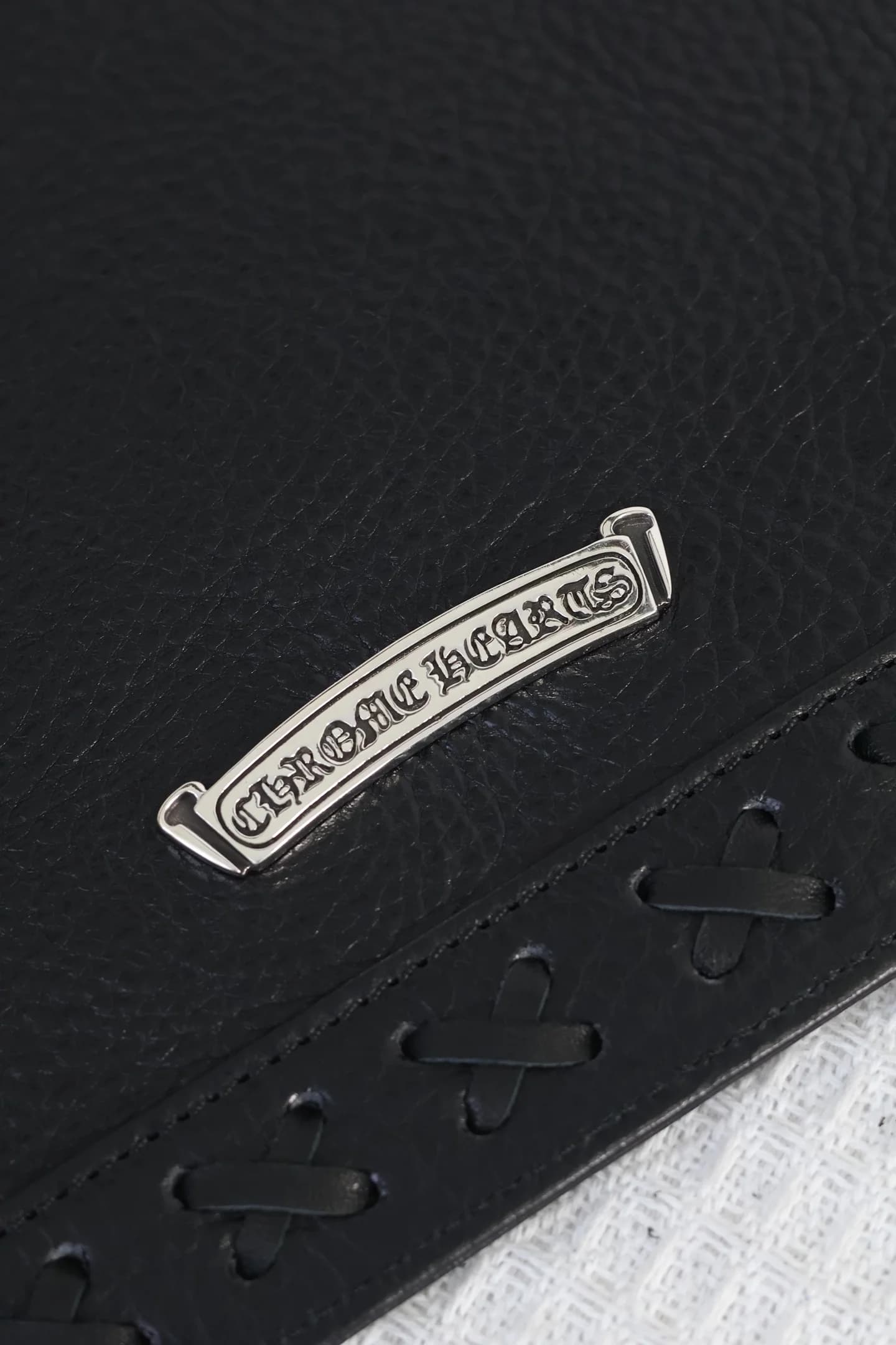 Крупный план серебряной планки с гравировкой Chrome Hearts и кожаной шнуровки
