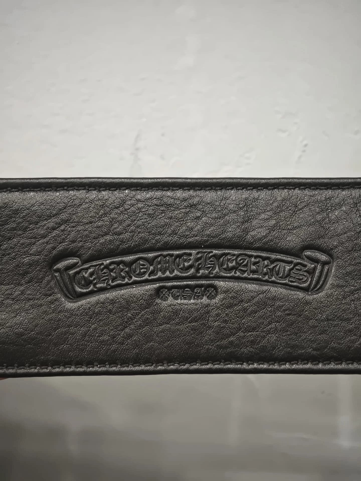 Фирменное тиснение логотипа-свитка Chrome Hearts на черной зернистой коже