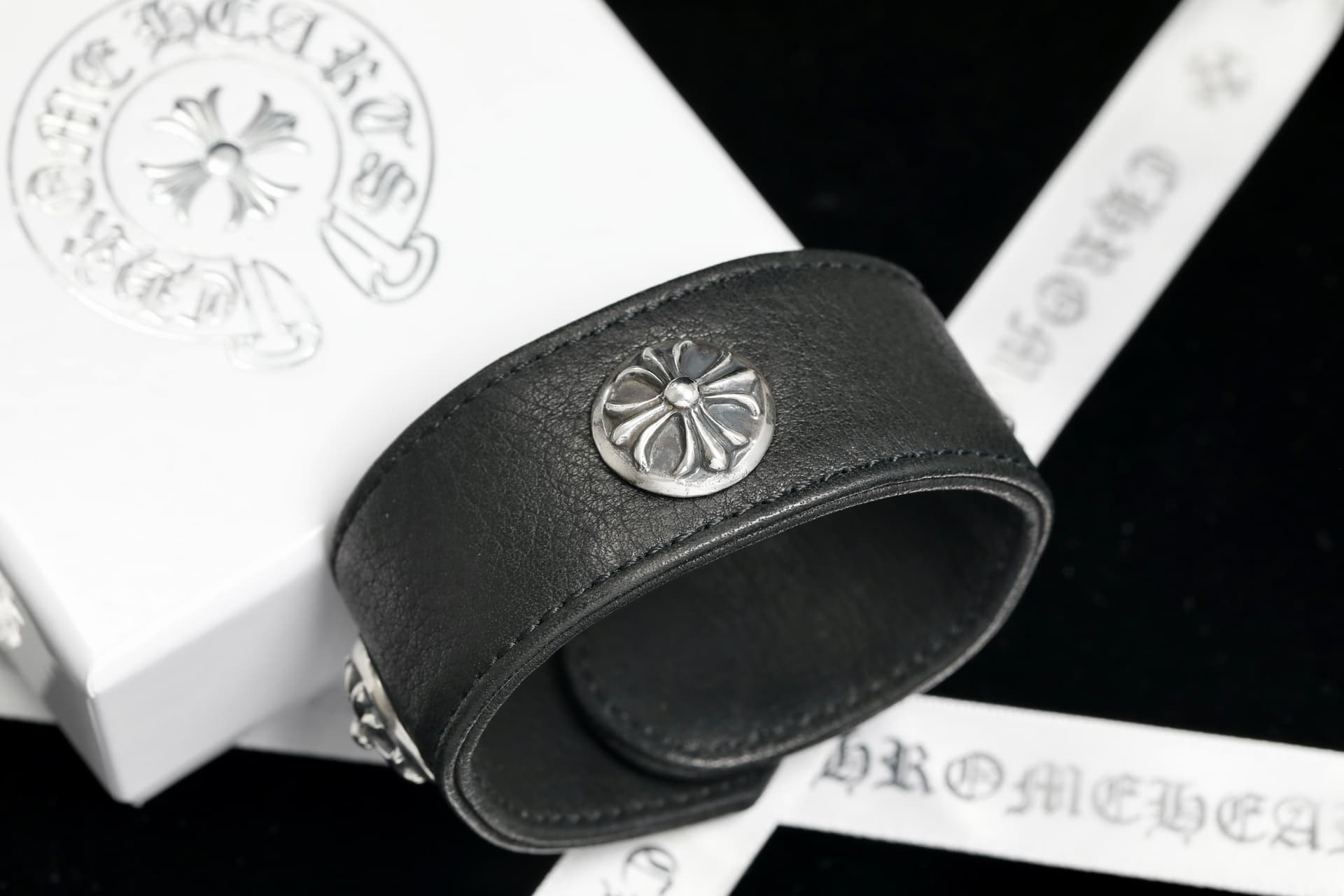 Широкий черный кожаный браслет Chrome Hearts с серебряной заклепкой Cross на фоне коробки