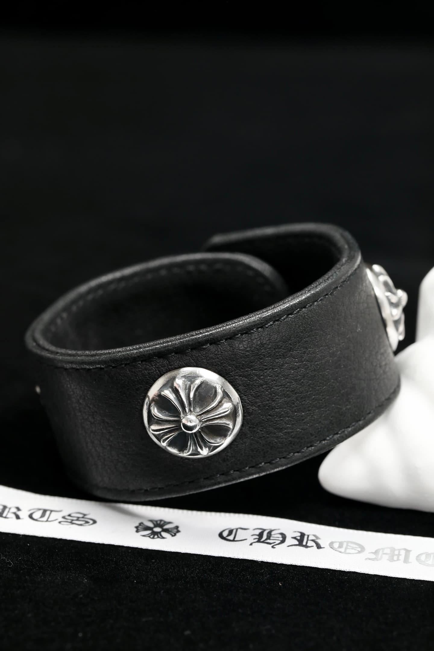 Вид сбоку на черный кожаный браслет Chrome Hearts с серебряным крестом