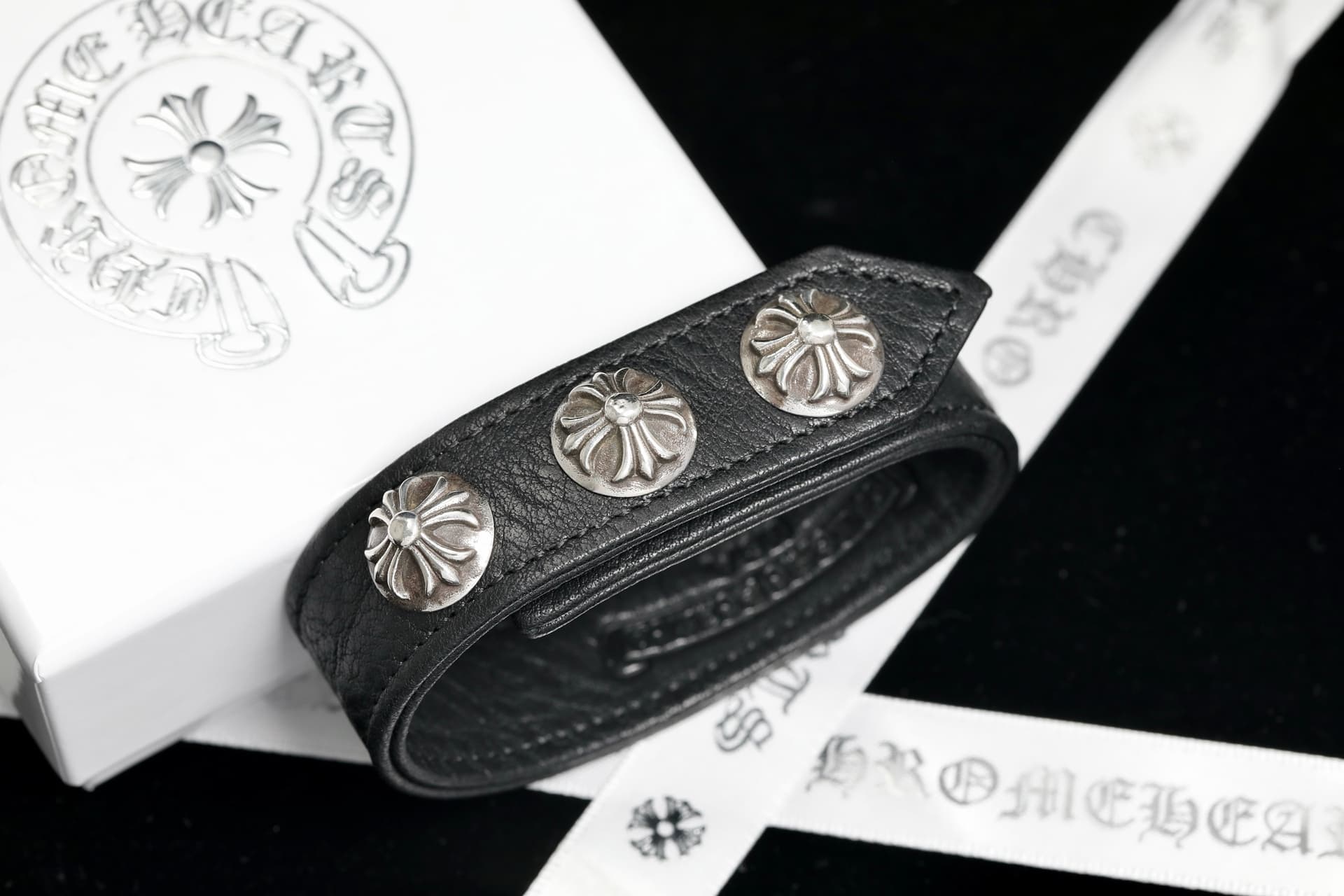 Черный кожаный браслет Chrome Hearts с серебряными заклепками на фоне упаковки