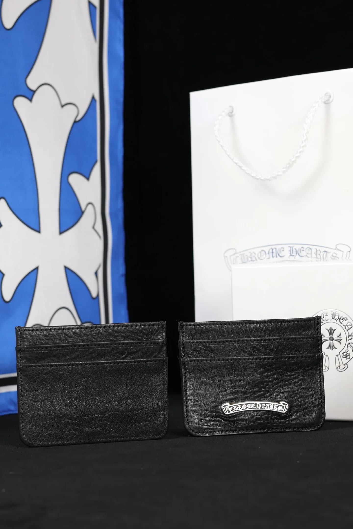 Два чёрных кожаных картхолдера Chrome Hearts на фоне фирменного пакета