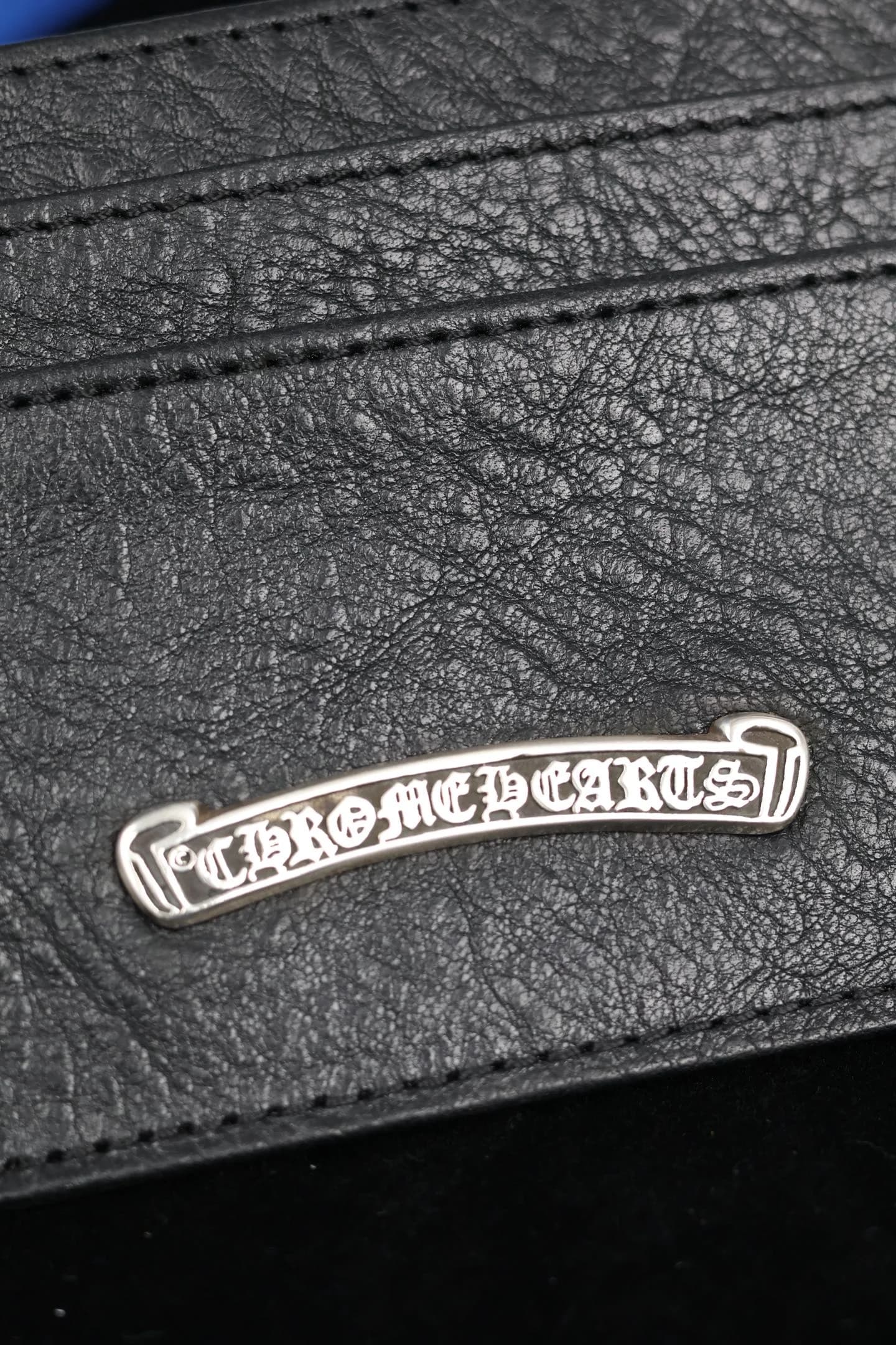 Крупный план фактурной кожи и серебряной плашки с гравировкой Chrome Hearts