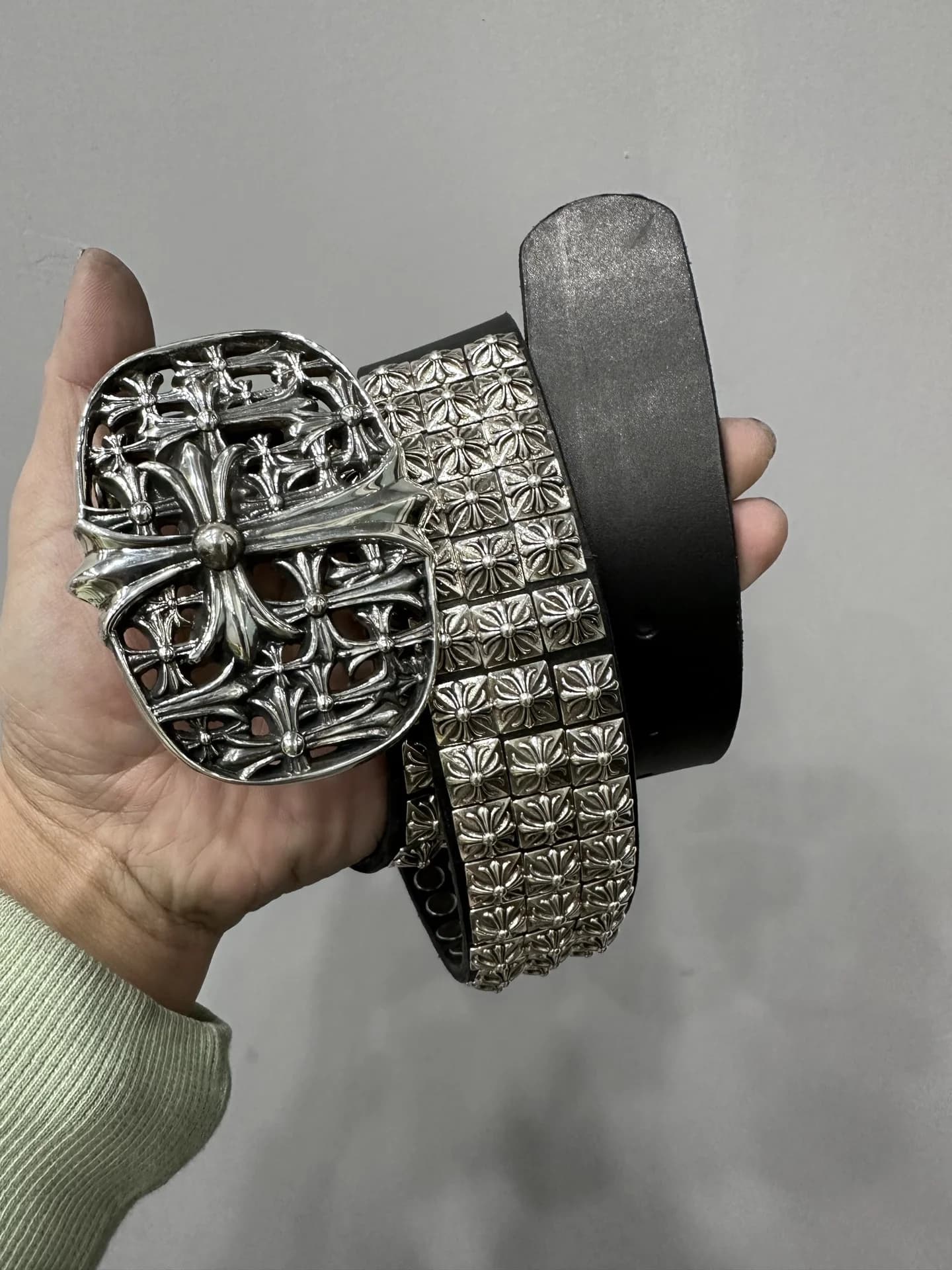 Свернутый черный кожаный ремень Chrome Hearts с массивной резной пряжкой в руке