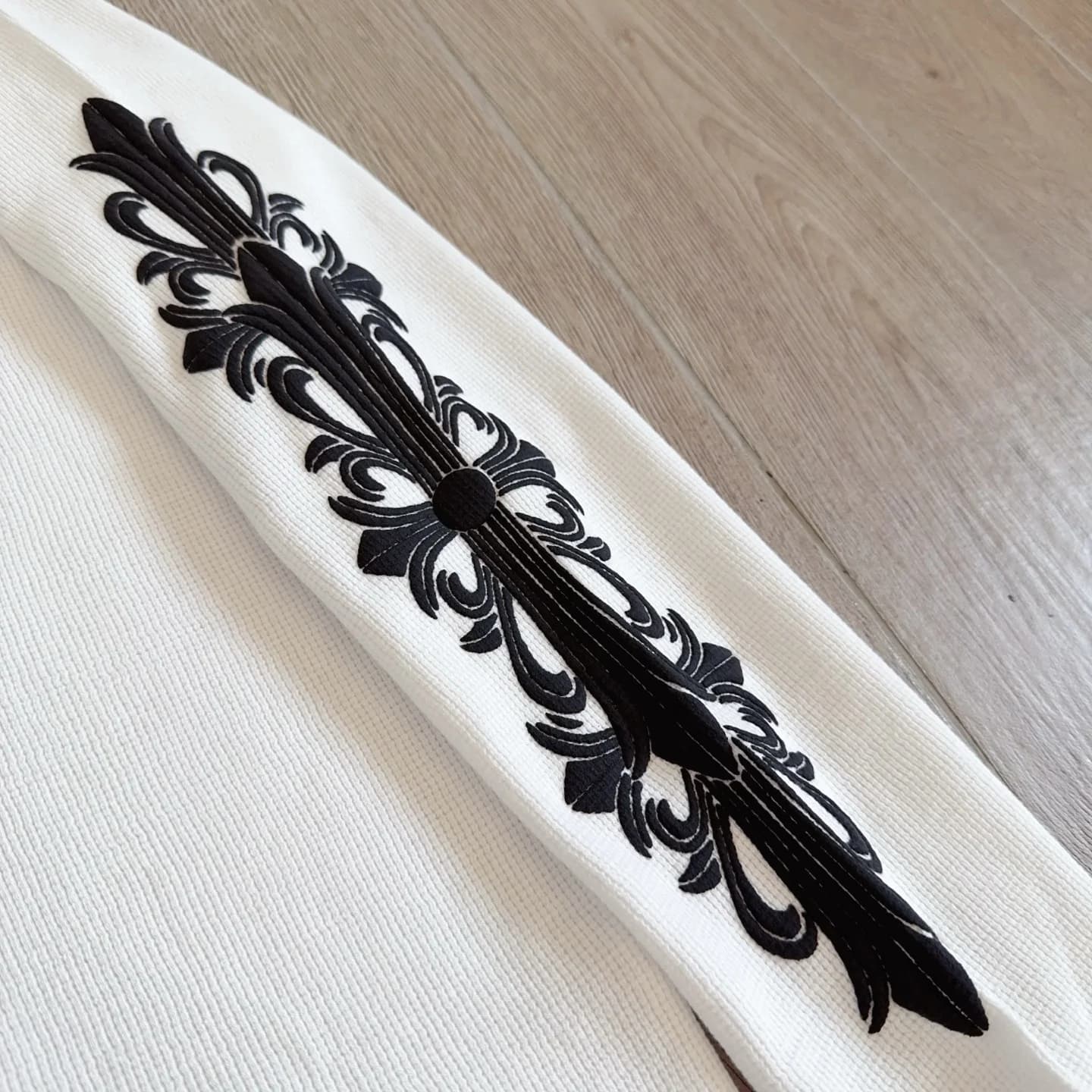 Крупный план нашивки с крестом на рукаве белого лонгслива Chrome Hearts