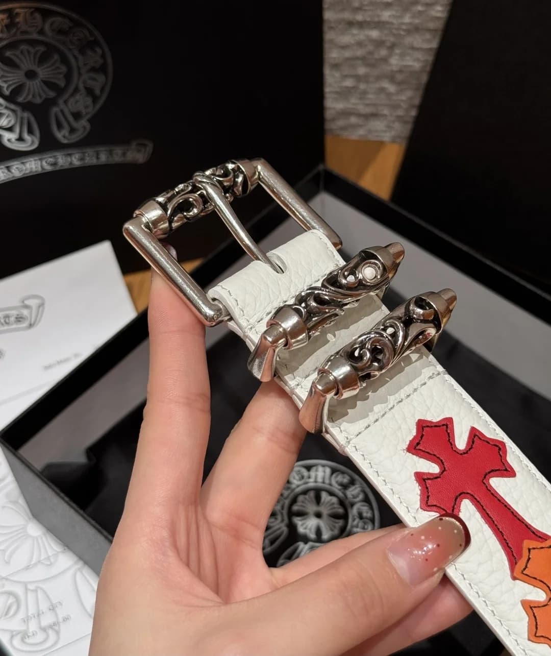 Крупный план серебряной роликовой пряжки и шлёвок на белом ремне Chrome Hearts