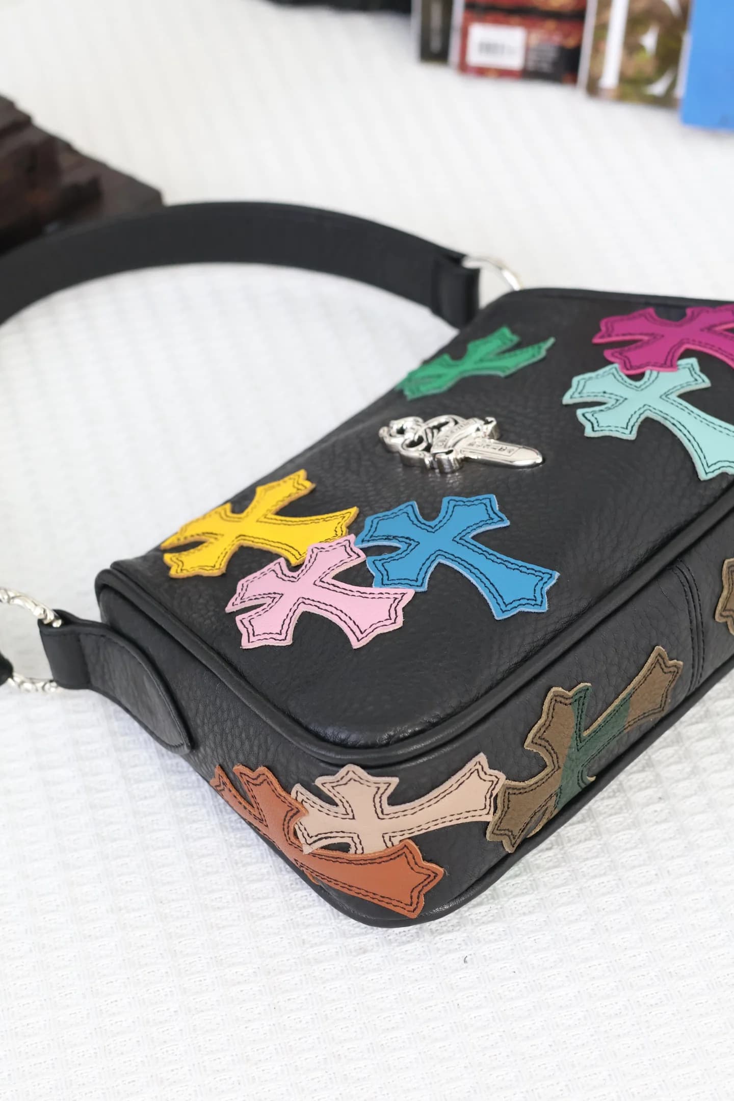 Верхний ракурс черной кожаной сумки Chrome Hearts с цветными нашивками и серебряным кинжалом