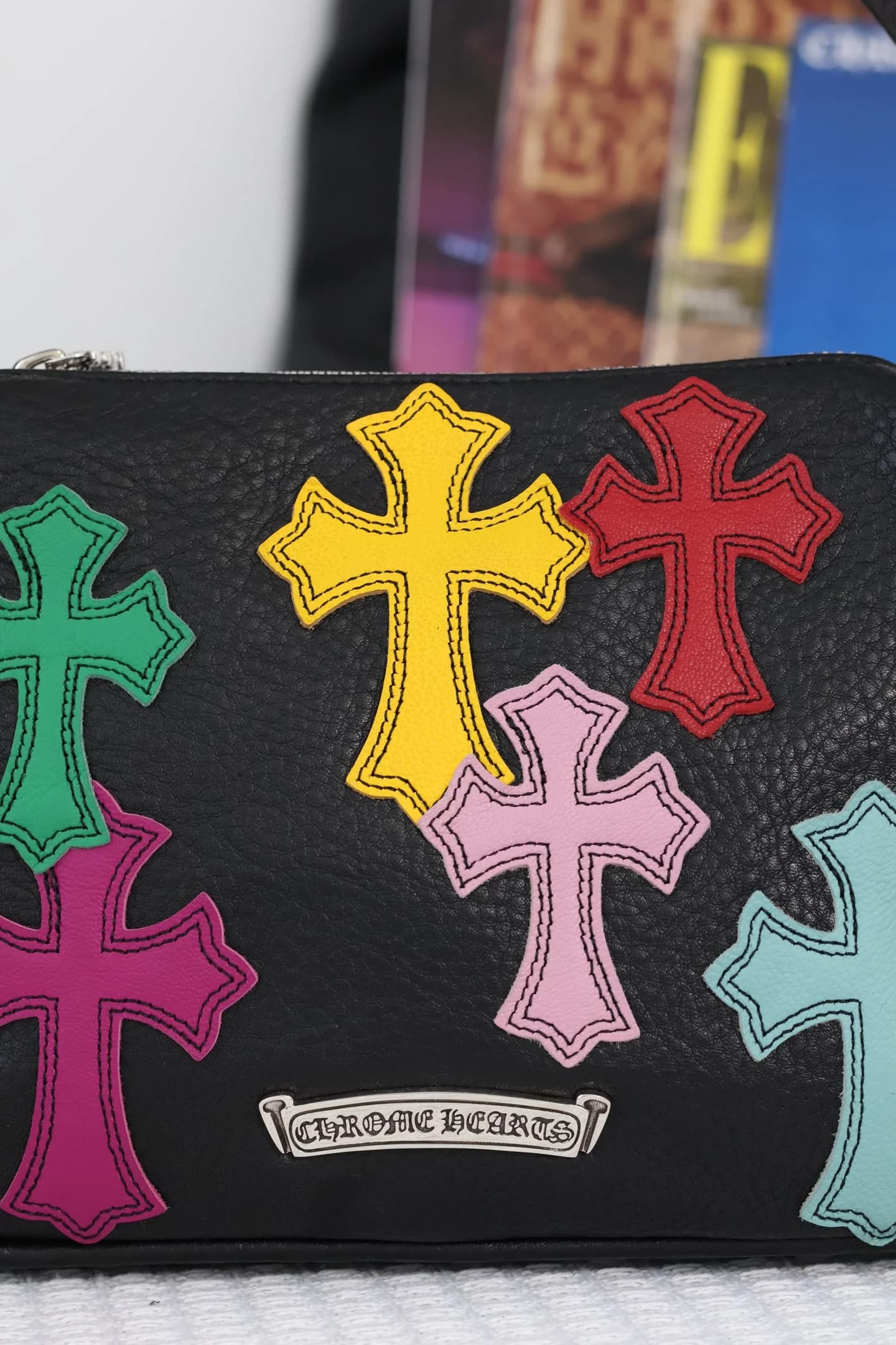 Крупный план задней стороны сумки Chrome Hearts с цветными крестами и серебряной пластиной с логотипом
