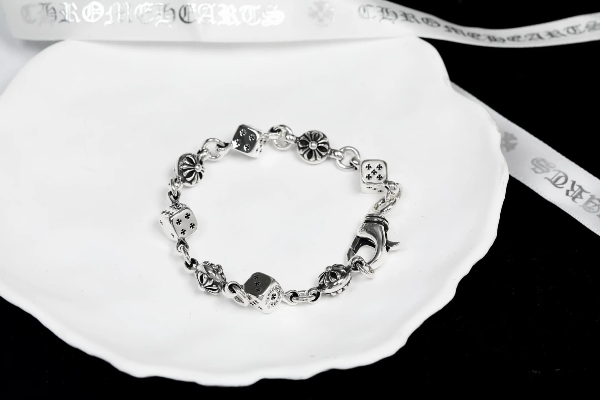 Серебряный браслет с игральными костями и крестами на белой тарелке