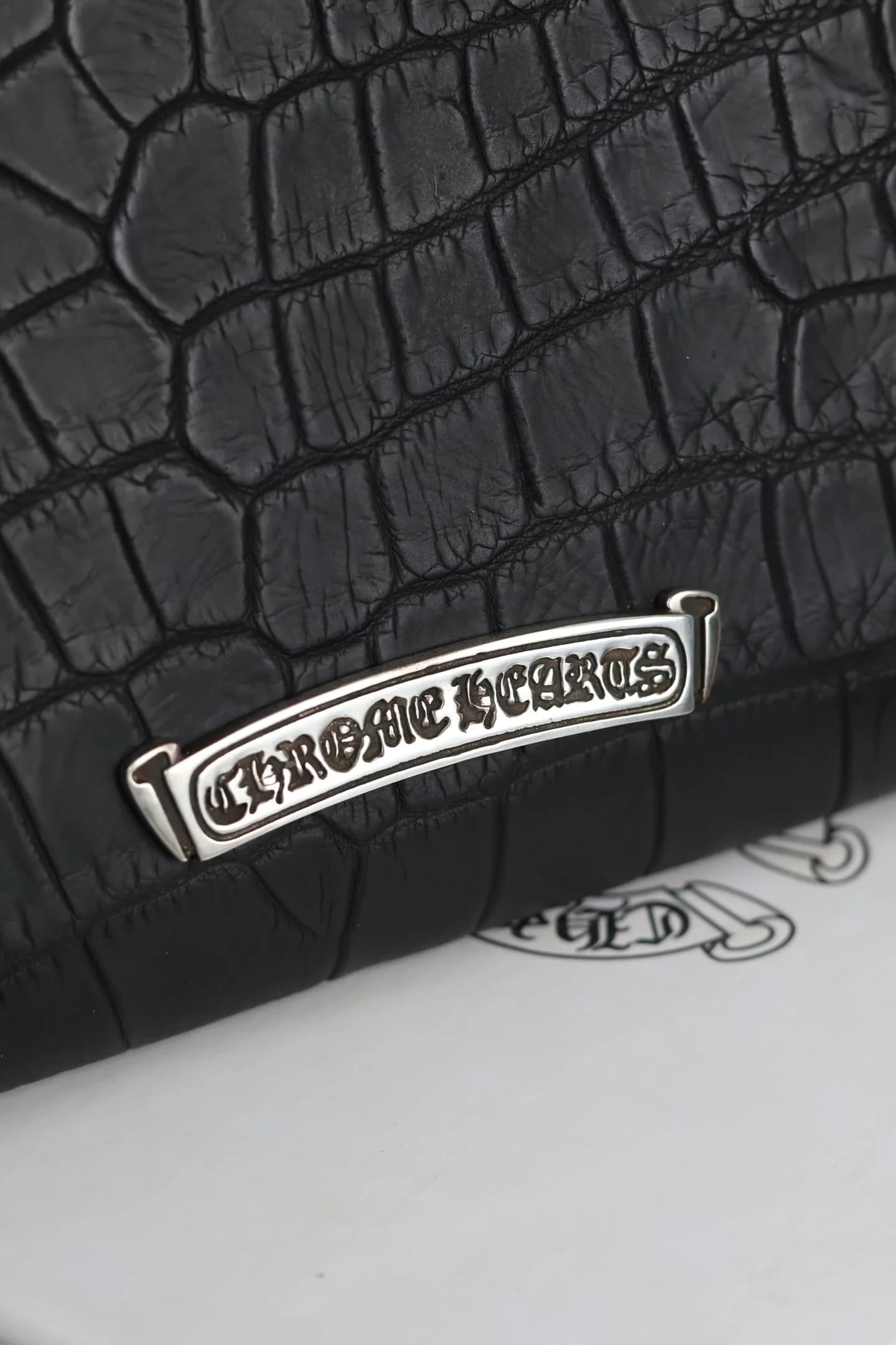 Деталь серебряной плашки с гравировкой Chrome Hearts на коже крокодила