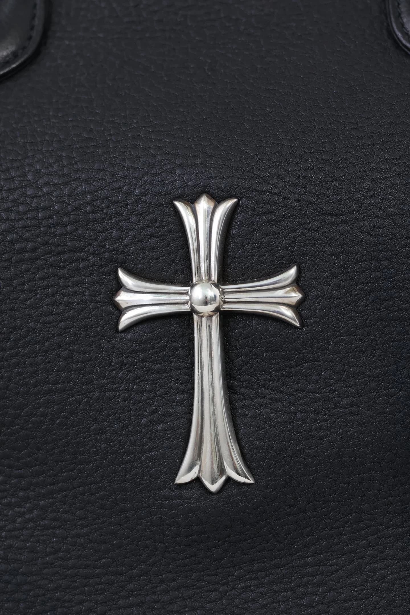 Крупный план серебряного креста Chrome Hearts на зернистой коже