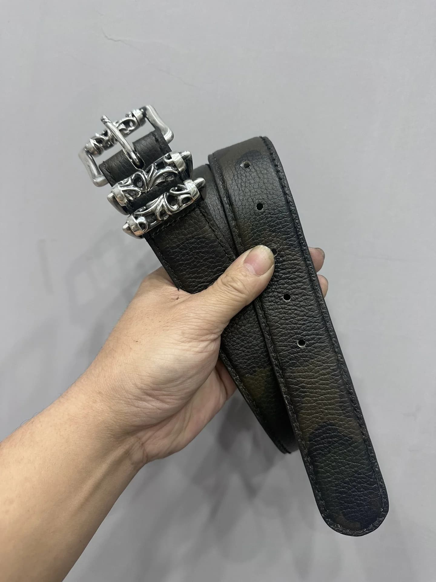 Свернутый камуфляжный ремень Chrome Hearts Roller в руке
