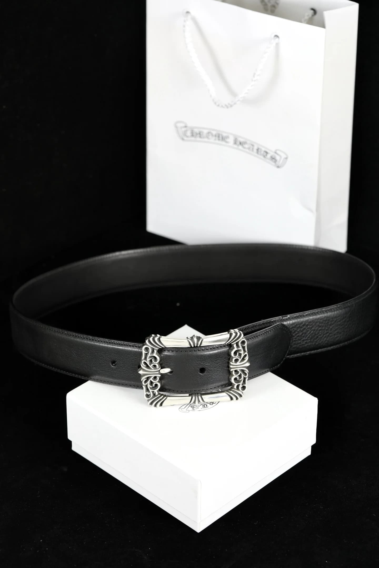 Черный кожаный ремень Chrome Hearts с фигурной серебряной пряжкой на фоне фирменной упаковки