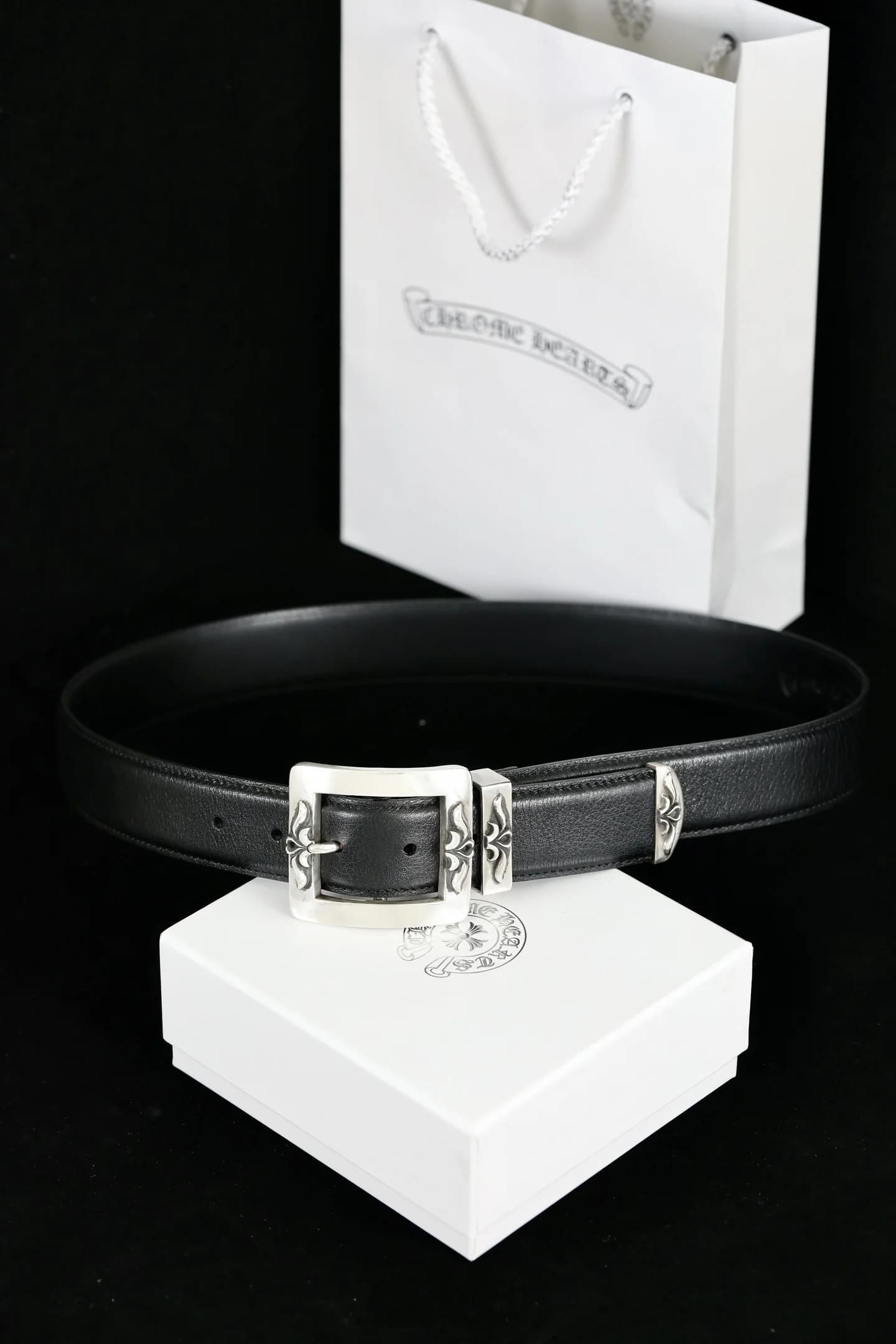 Черный кожаный ремень Chrome Hearts с серебряной пряжкой на фоне фирменной коробки и пакета