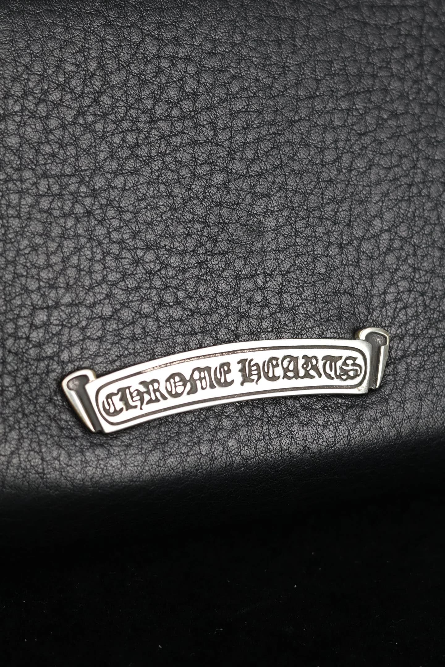 Крупный план серебряной плакетки с надписью Chrome Hearts на коже