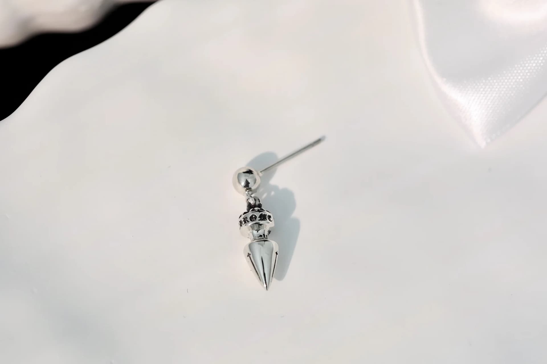 Одиночная серьга Chrome Hearts с конической подвеской на белой рельефной поверхности