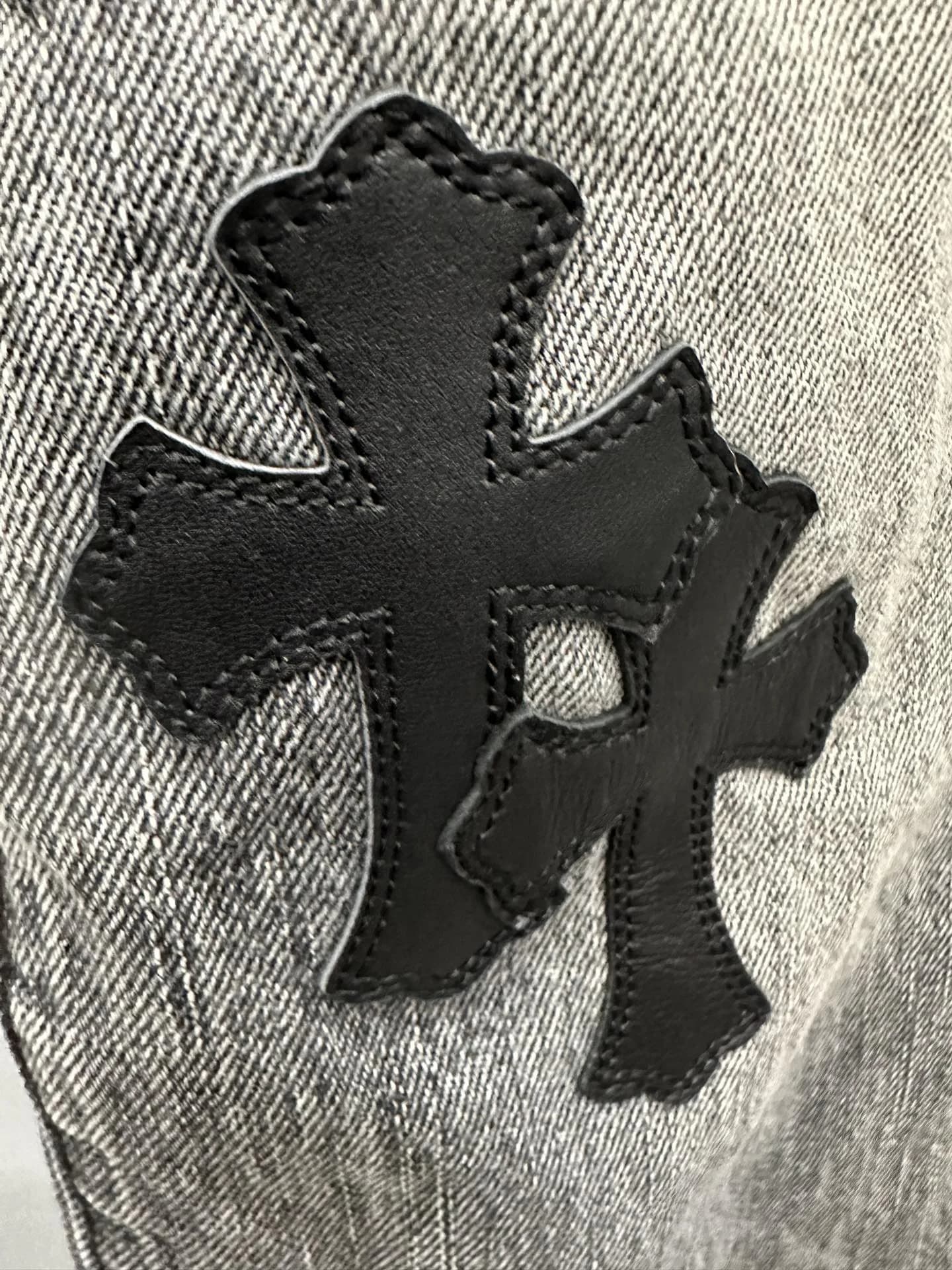 Крупный план нашивок-крестов из черной кожи на джинсах Chrome Hearts