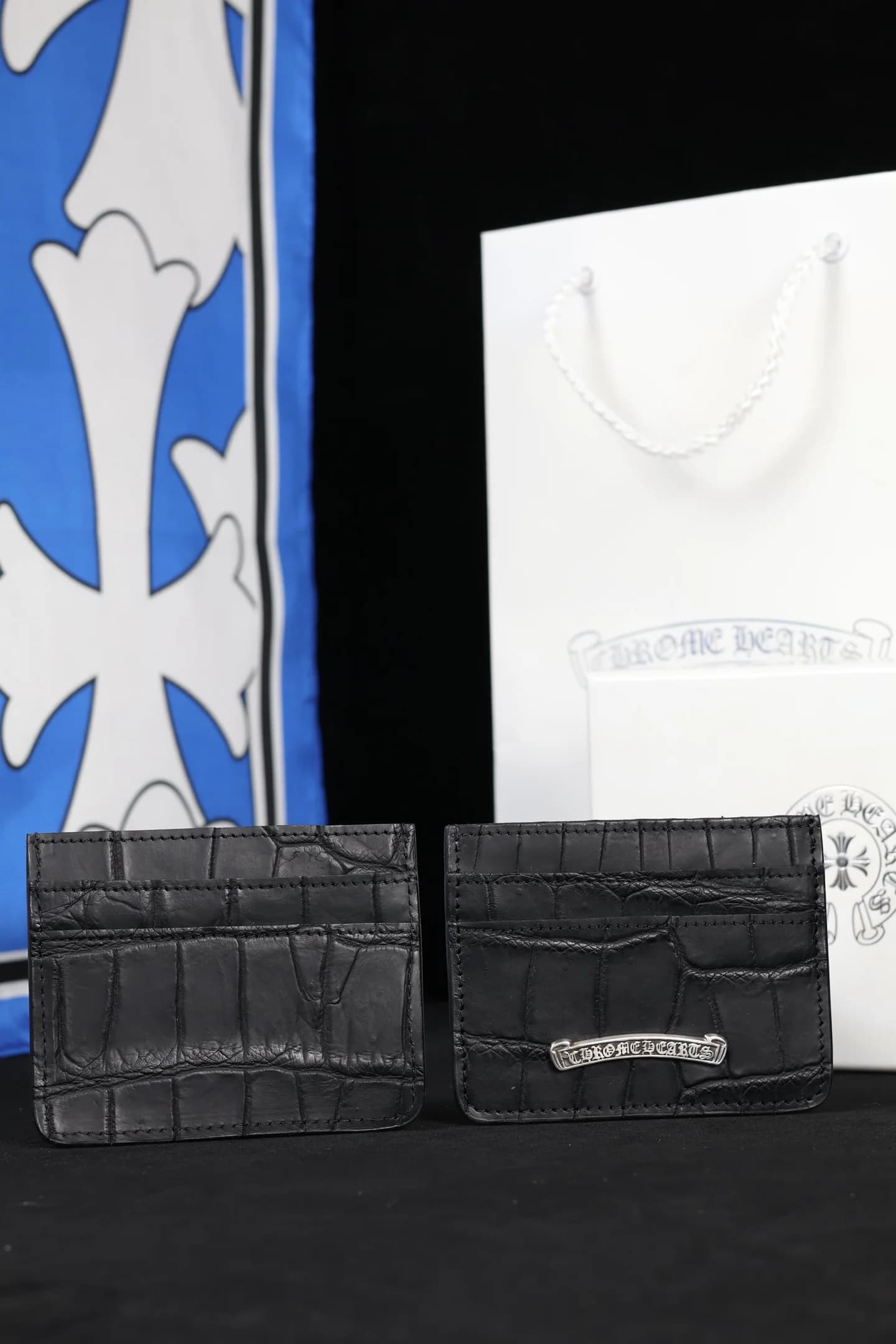 Два черных картхолдера Chrome Hearts из кожи крокодила на фоне фирменного пакета