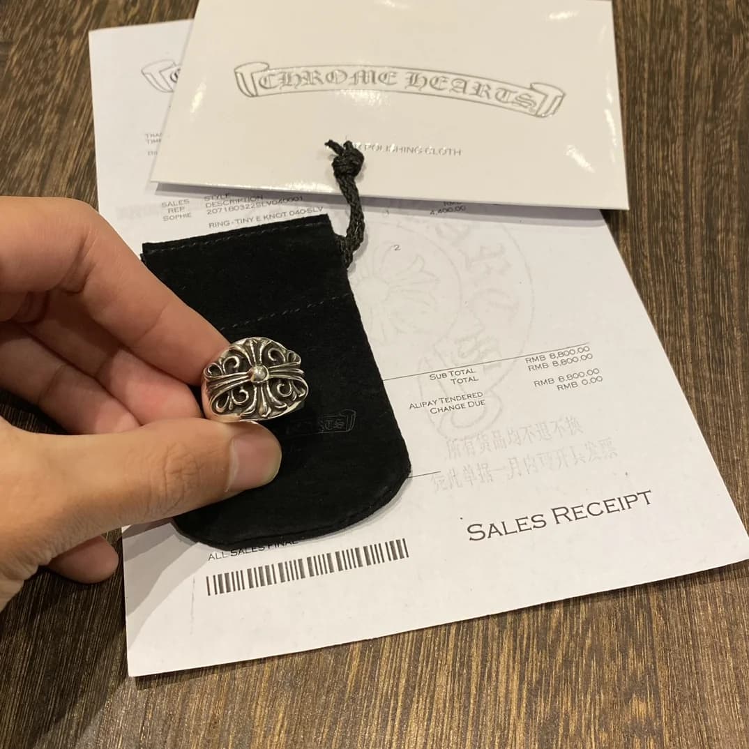 Серебряное кольцо Chrome Hearts Keeper в руке на фоне пыльника и чека
