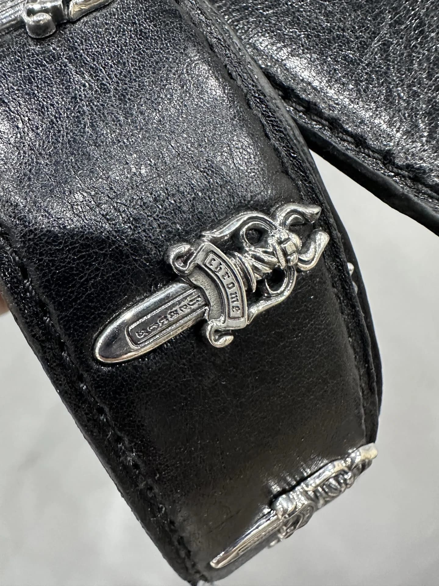 Крупный план серебряной заклепки Dagger на черной коже ремня Chrome Hearts