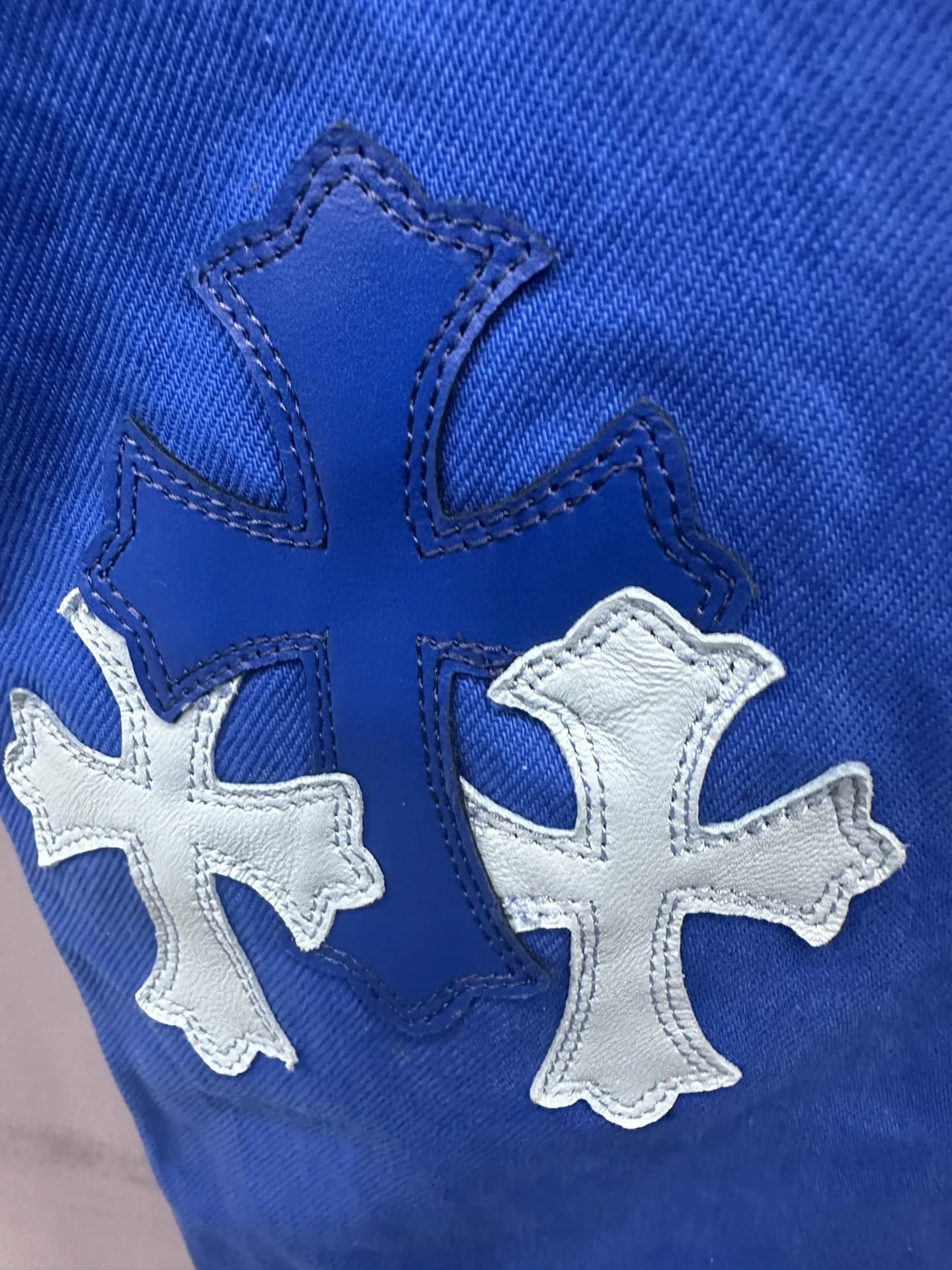 Кожаные нашивки-кресты синего и белого цвета на штанине джинсов Chrome Hearts