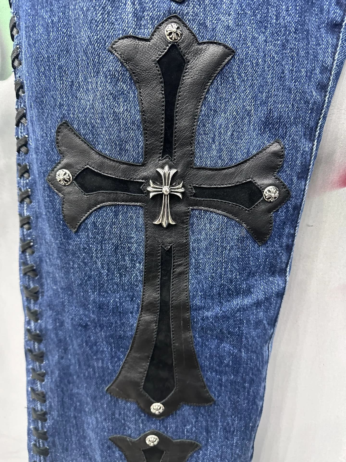 Кожаный патч в виде креста с серебряной деталью на джинсах Chrome Hearts, крупный план