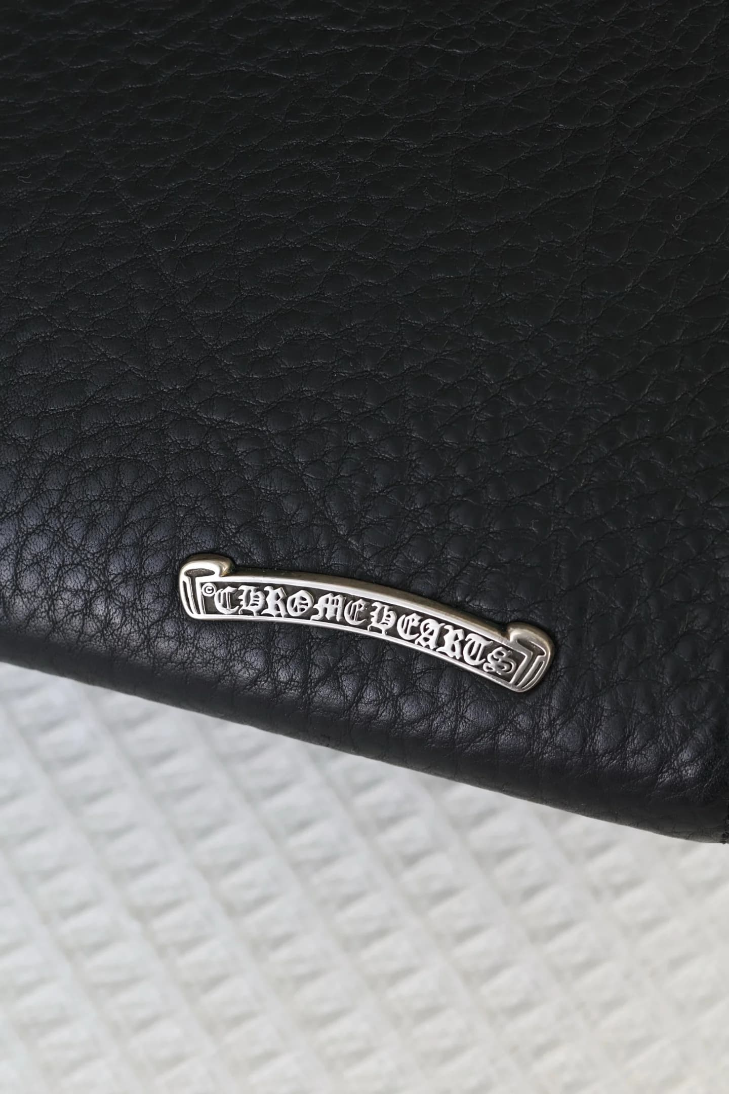Крупный план серебряной плашки с гравировкой Chrome Hearts Scroll Logo
