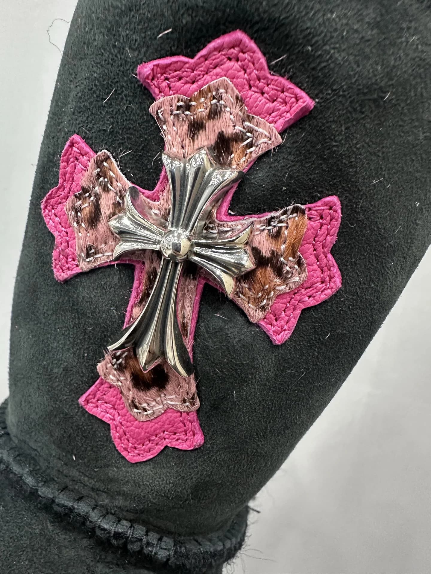Деталь декора сапог Chrome Hearts x UGG Classic: серебряный крест на леопардовой нашивке с розовой окантовкой
