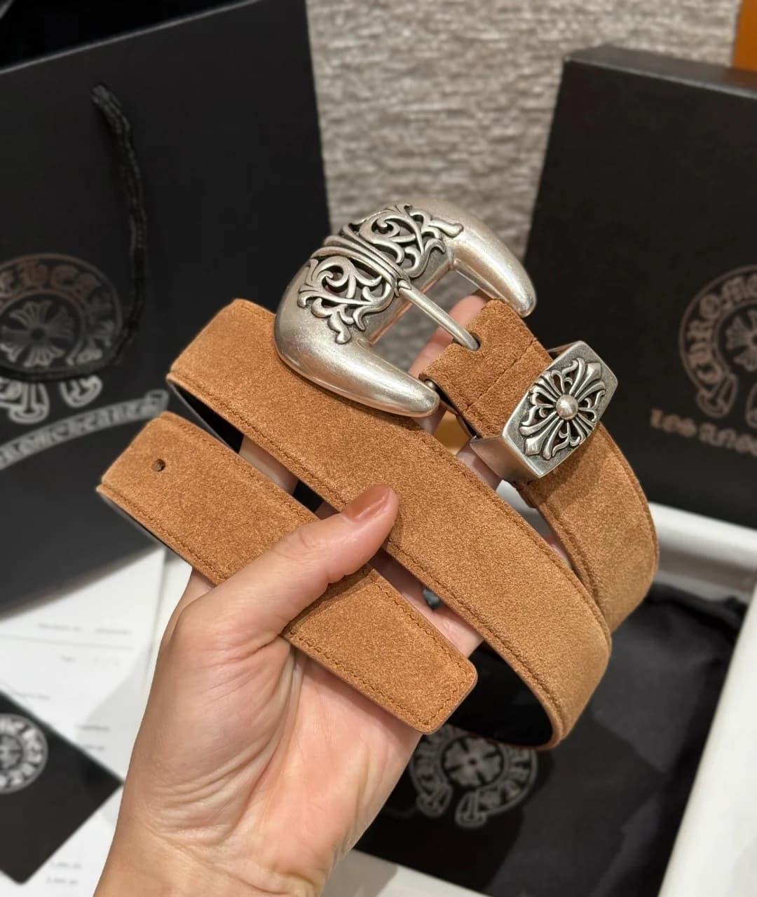 Свернутый замшевый ремень Chrome Hearts с металлической пряжкой в руке