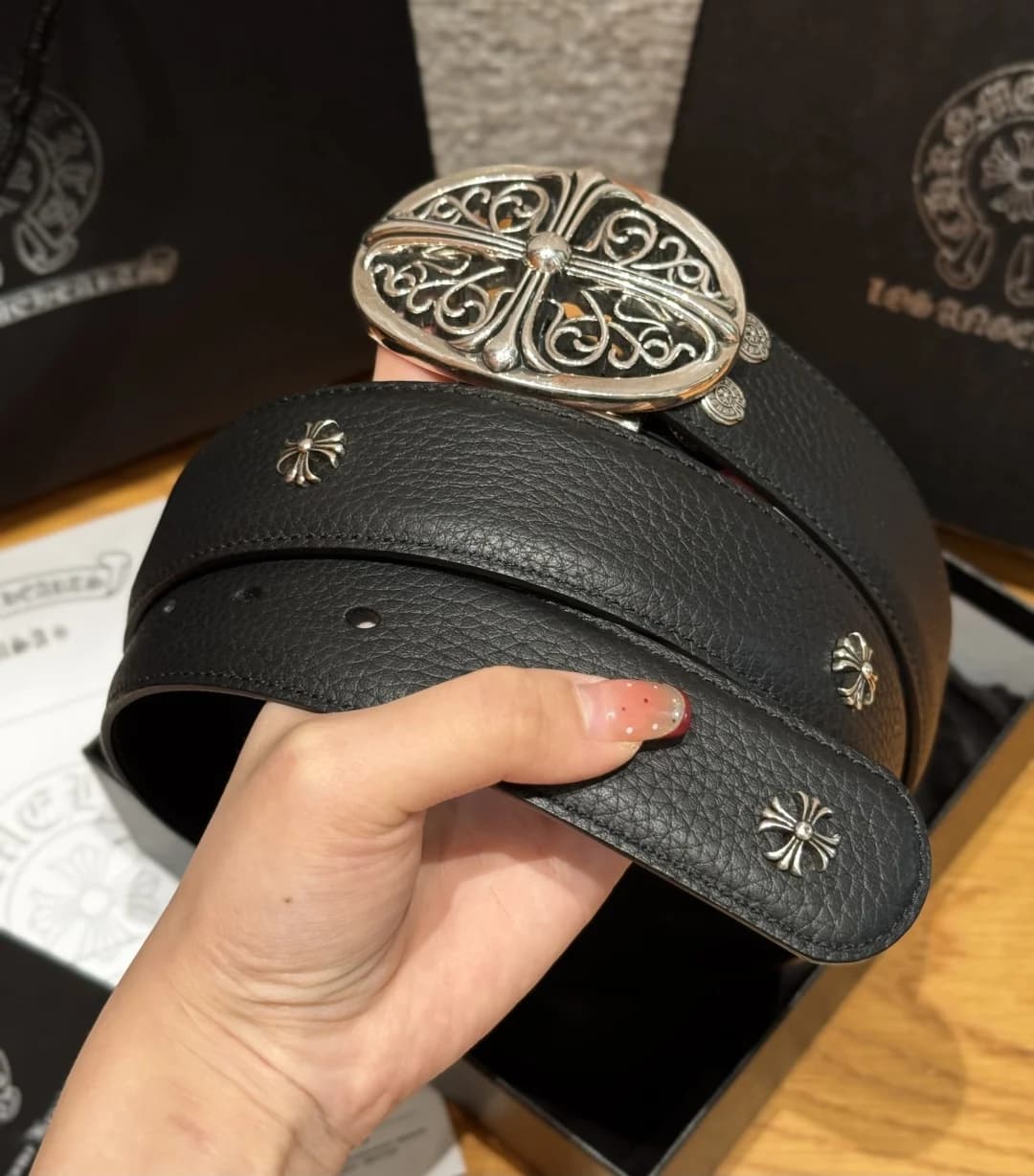 Свернутый кожаный ремень Chrome Hearts с заклепками-крестами и овальной пряжкой в руке