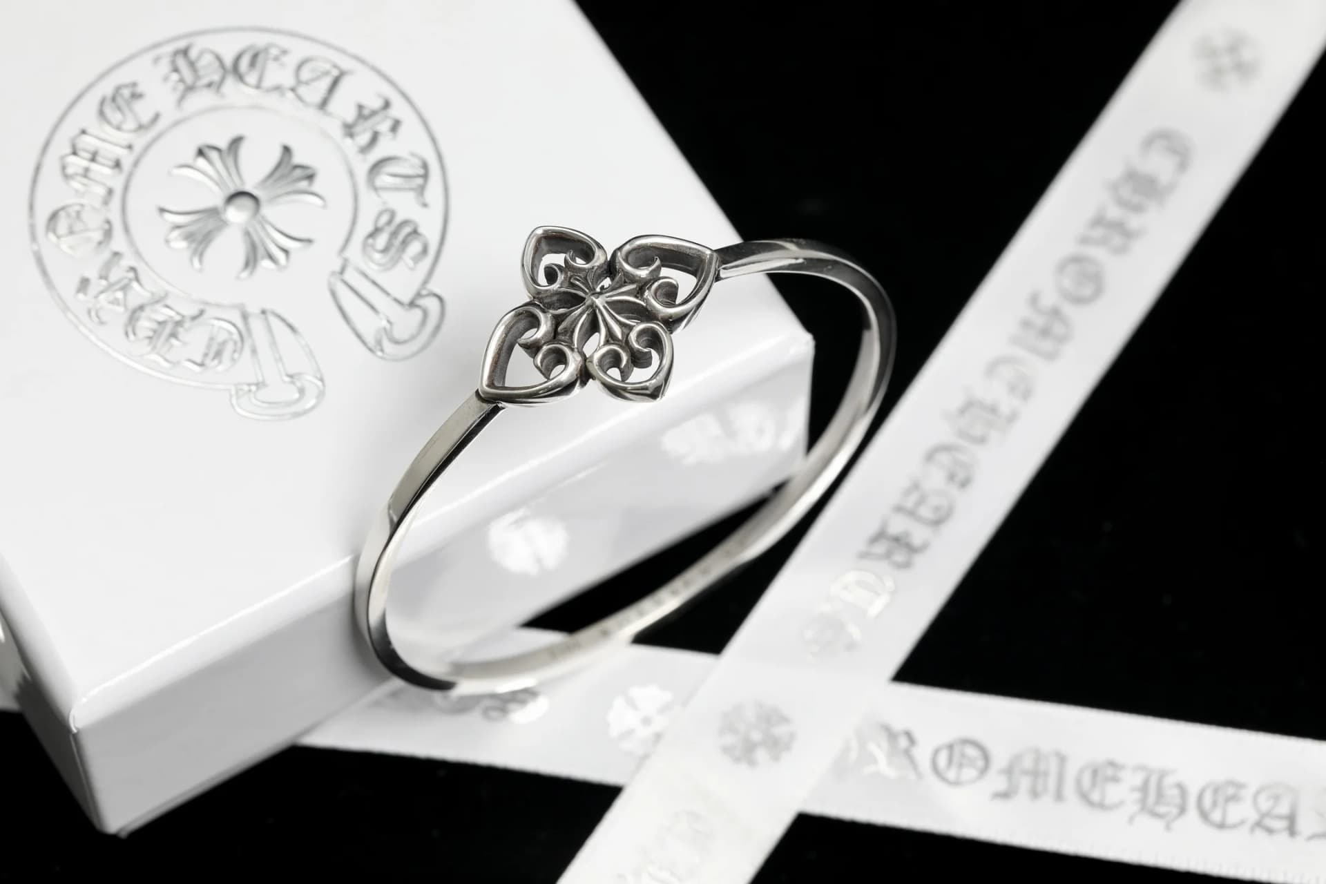 Жесткий серебряный браслет на фоне фирменной коробки и ленты Chrome Hearts