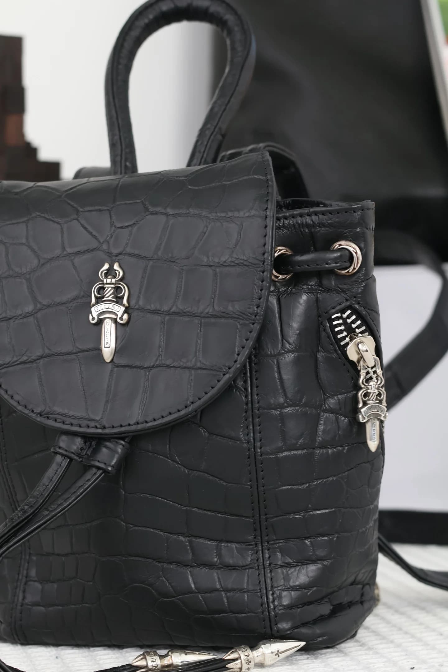 Крупный план клапана и бокового кармана рюкзака с серебряным кинжалом Chrome Hearts