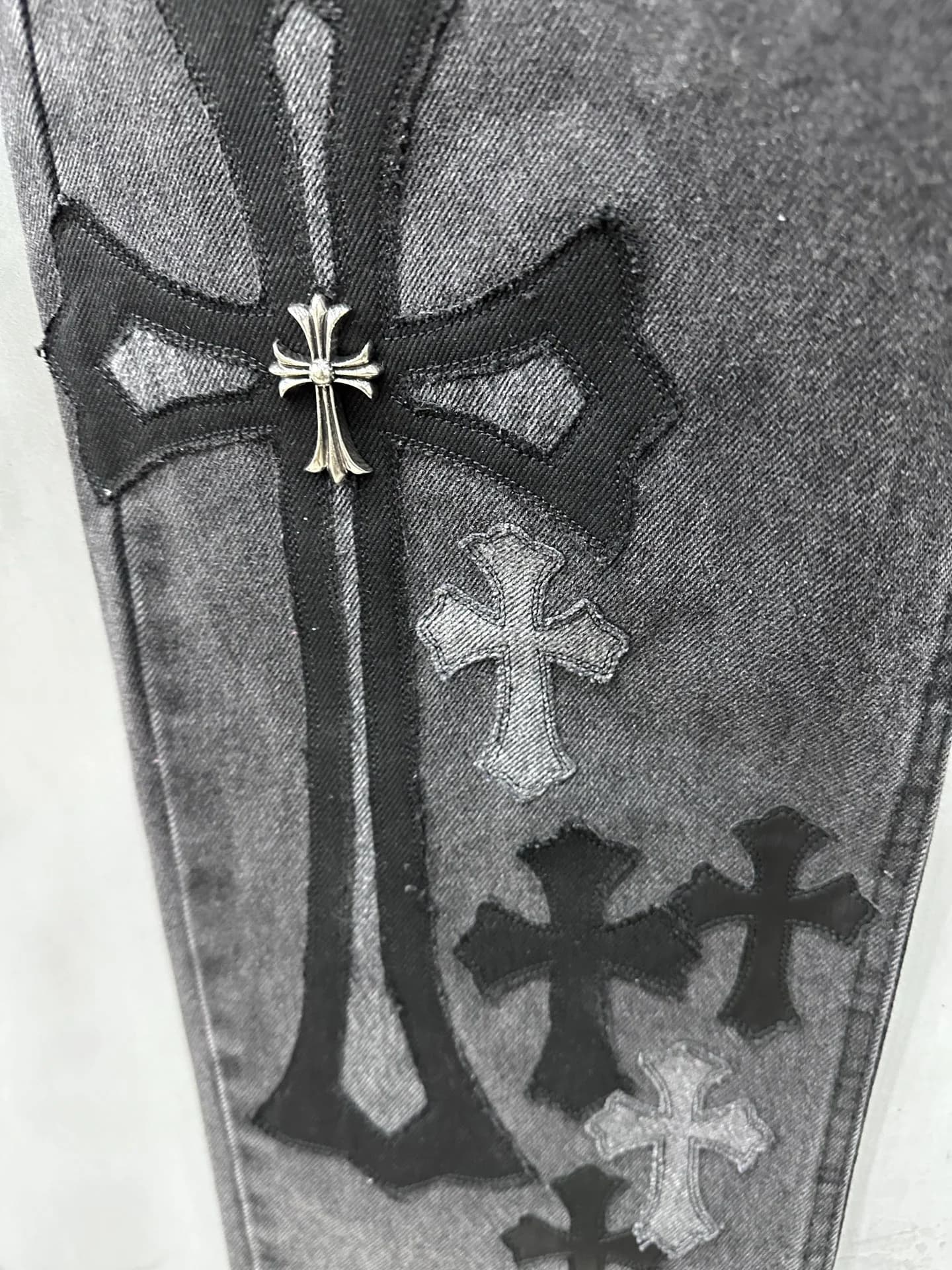 Декоративный серебряный крест поверх кожаной нашивки на джинсах Chrome Hearts