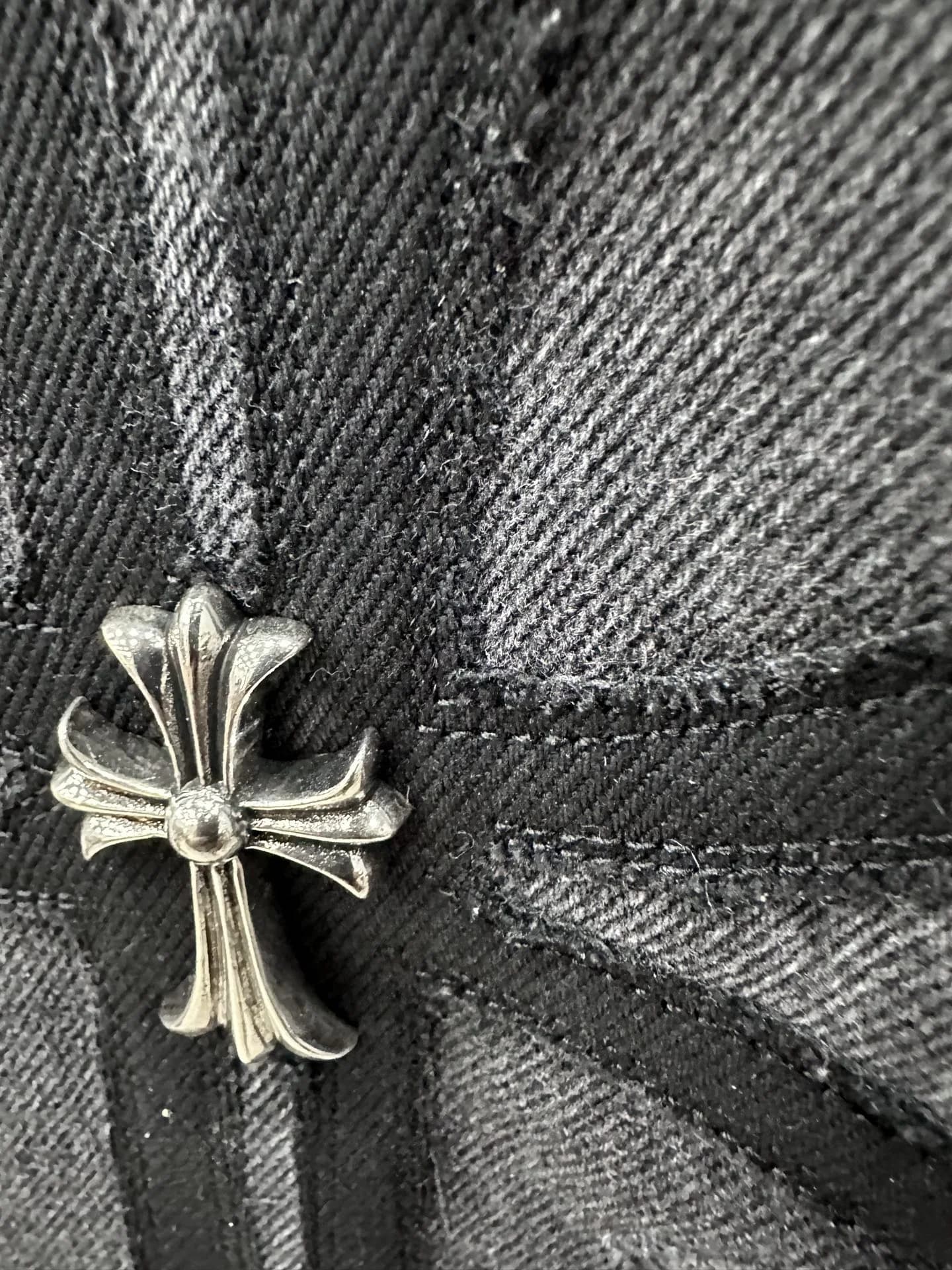 Крупный план серебряного креста Chrome Hearts на джинсах