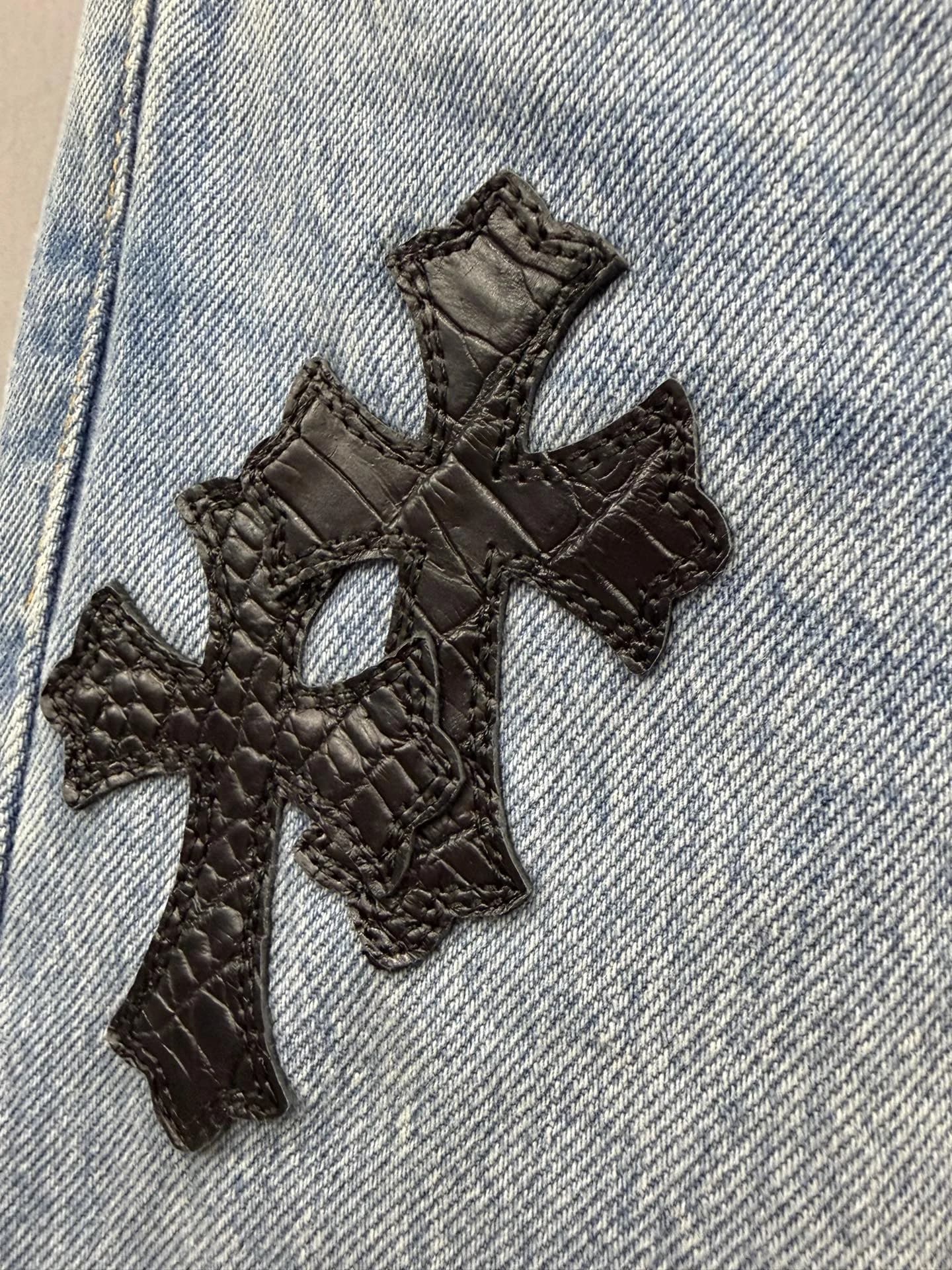 Деталь нашивки в виде креста из черной кожи крокодила на джинсах Chrome Hearts x Levi's 501