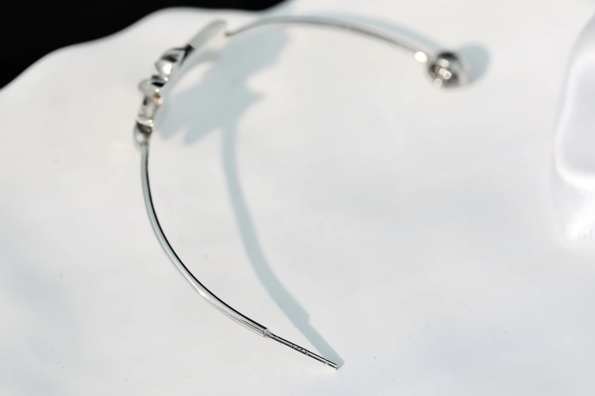 Серебряная серьга Chrome Hearts на светлом фоне, вид сверху