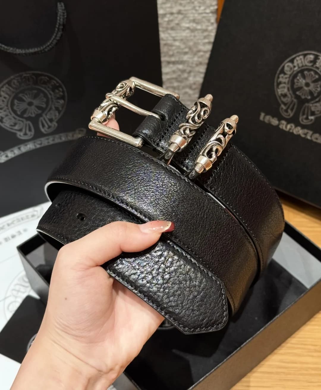 Свернутый черный кожаный ремень Chrome Hearts с серебряной пряжкой в руке