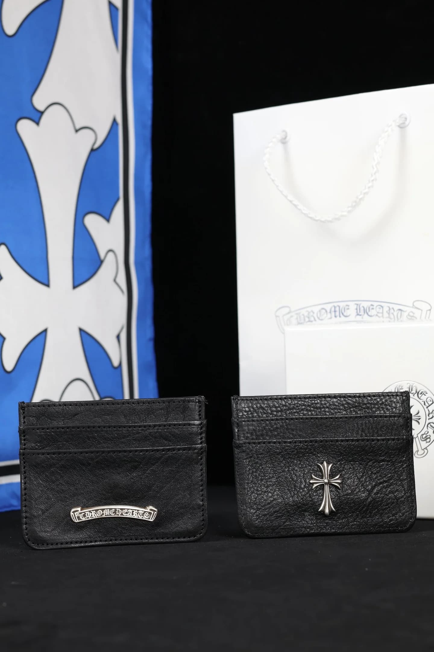 Два черных кожаных картхолдера Chrome Hearts на фоне подарочного пакета